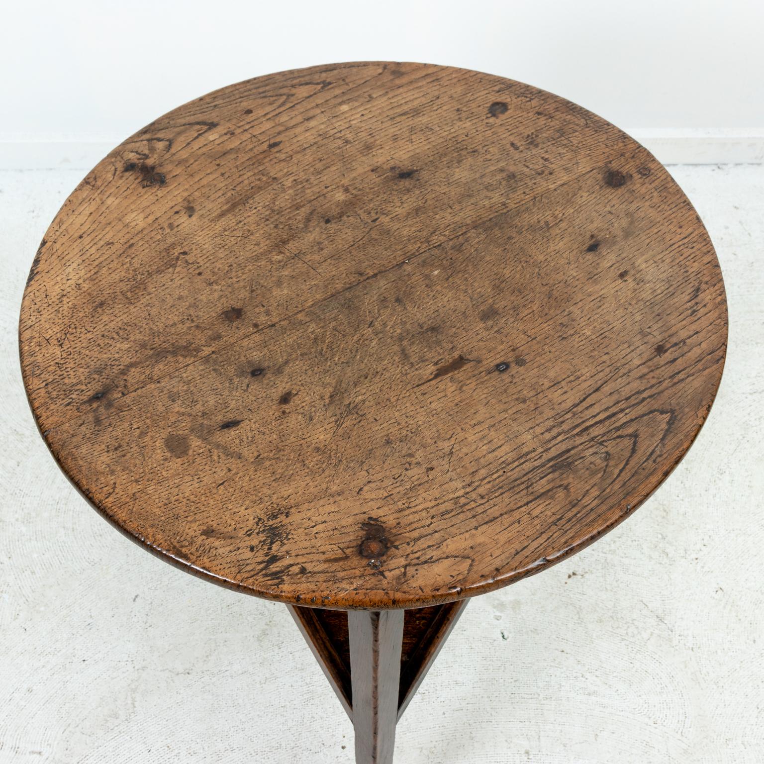 English style cricket table in a rough hewn finish, circa 18th century. The piece also features a bottom triangular shaped shelf. Please note of wear consistent with age including minor wood loss, scratches, and chips due to daily use.