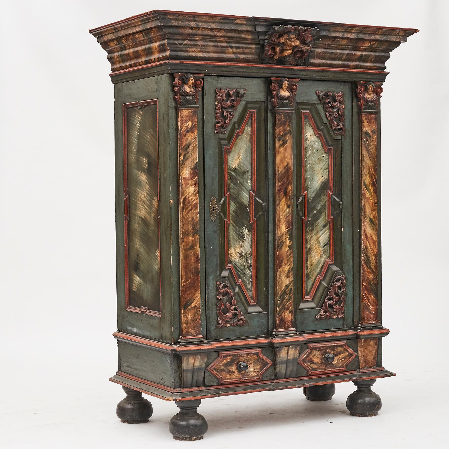 A Danish 18th century baroque cabinet with rich carved wood details.

Features a nicely molded and overhung cornice, with small putti (angle) wrapped within acanthus leaves, carved prominently at center.
Columns on either side and in middle with