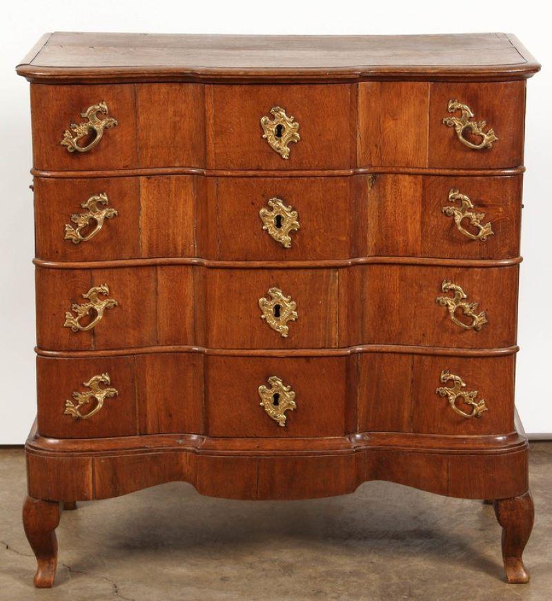 A late 18th century Danish Baroque oak chest with breakfront top over a case with four drawers mounted with elaborate gilt metal hardware, raised on short cabriole legs. The side panels each mounted with a handle for transport.