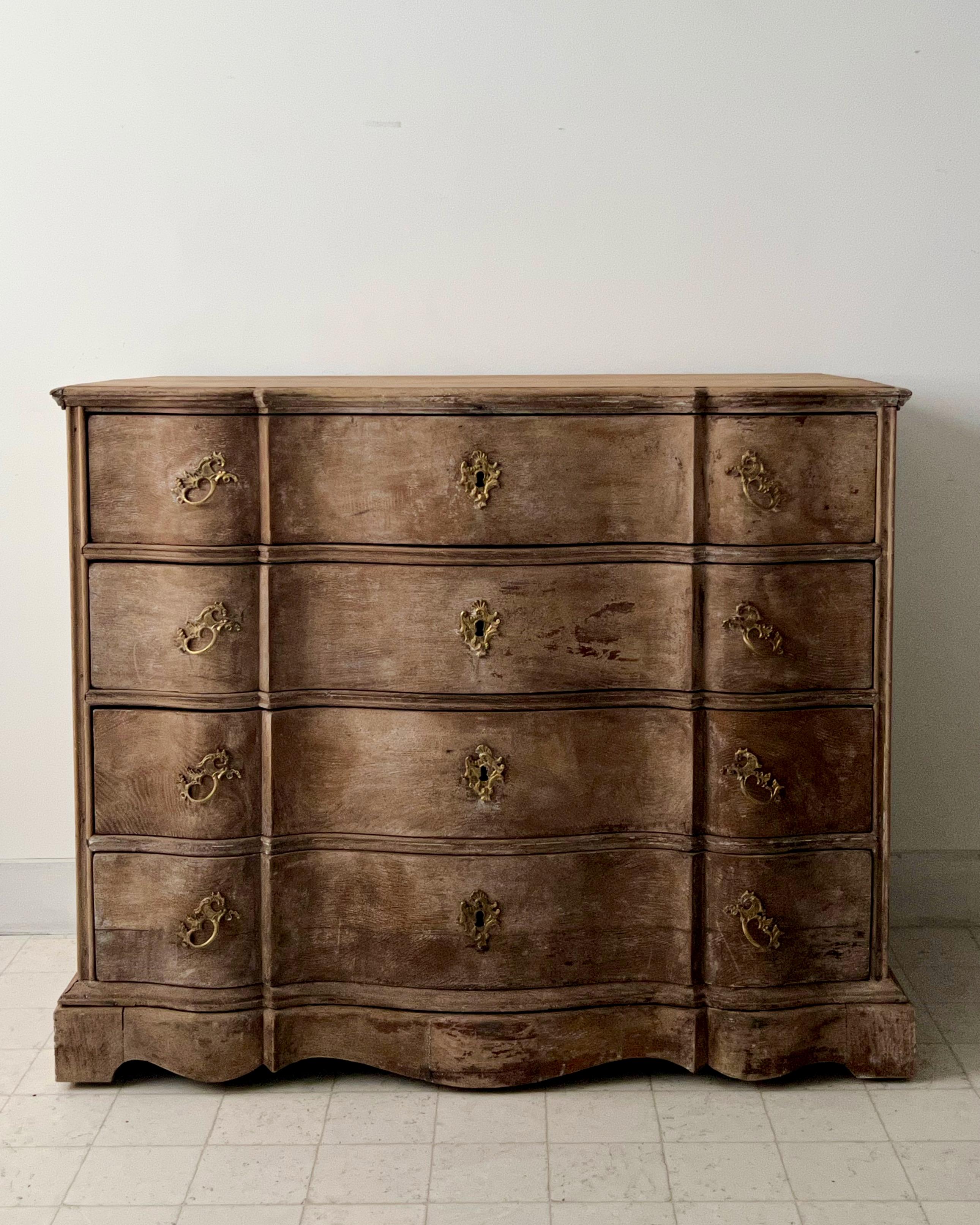 18th century Danish chest of drawers in richly carved bleached oak with curvaceous serpentine drawer fronts with handsome original bronze hardwares and shaped top, handsome original large iron handles on the side panels and beautifully carved apron