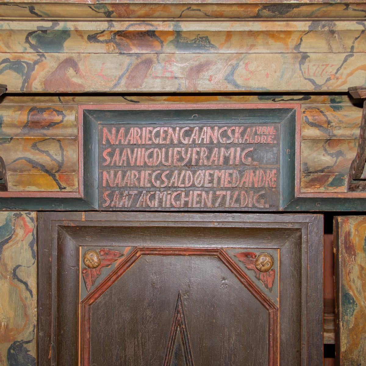 A large Danish painted court cabinet with two doors revealing shelving. Underneath the doors are two drawers. The top of the cabinet is adorned with a story in a Nordic language possibly regarding river deities. The cabinet has carved faces and
