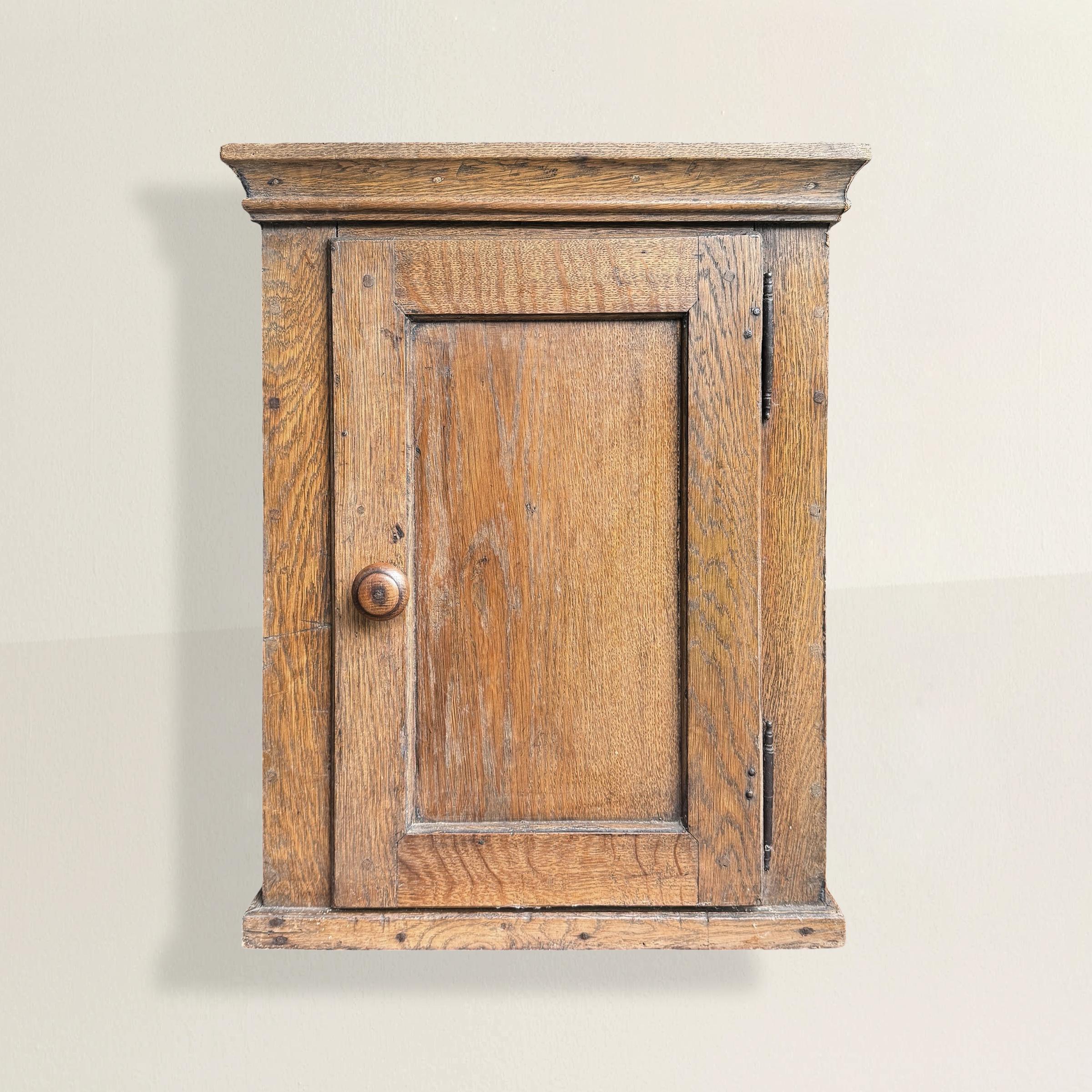 Modeste vestige de la vie quotidienne, cette armoire de cuisine danoise du XVIIIe siècle porte l'autorité tranquille de l'usage et de la survie. Construit en chêne et fixé au mur, il n'a jamais été conçu pour impressionner, mais seulement pour