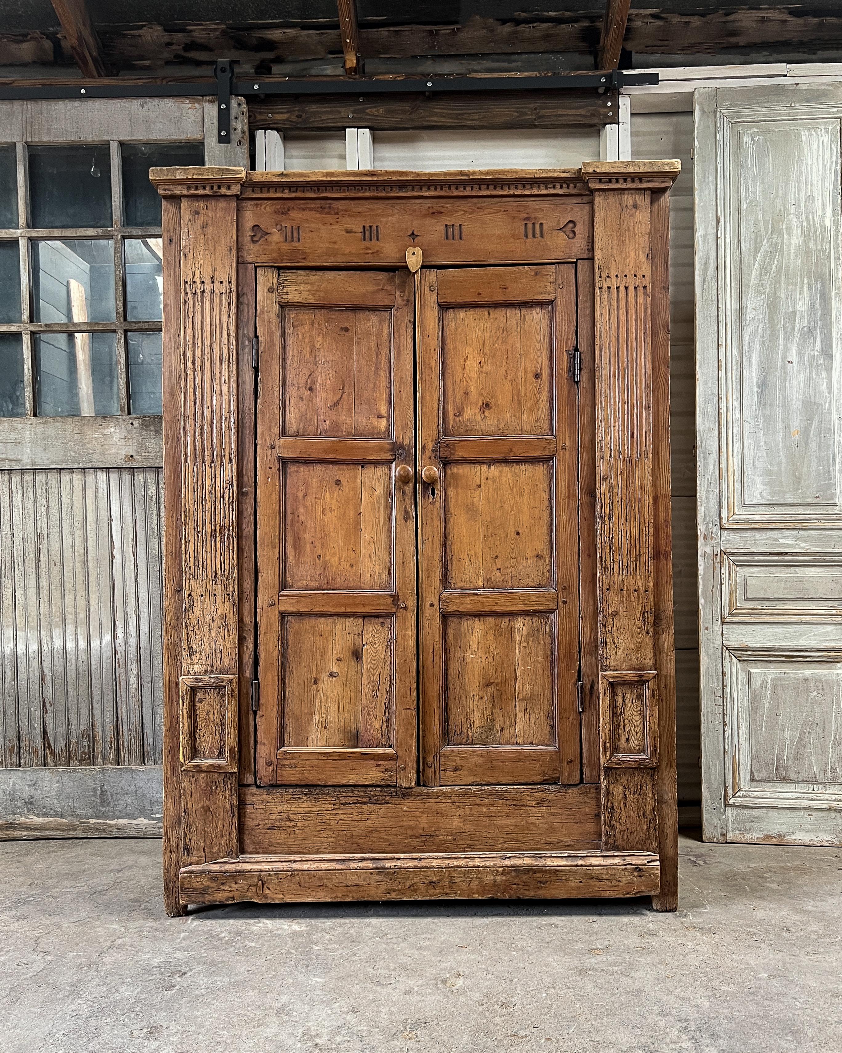 Large, authentic antique solid pine armoire found in The Netherlands. Dating to the late 18th century, the armoire is constructed utilizing pegged joinery. Hand-carved details on the front including dentil molding, hearts, fluted column-like panels,