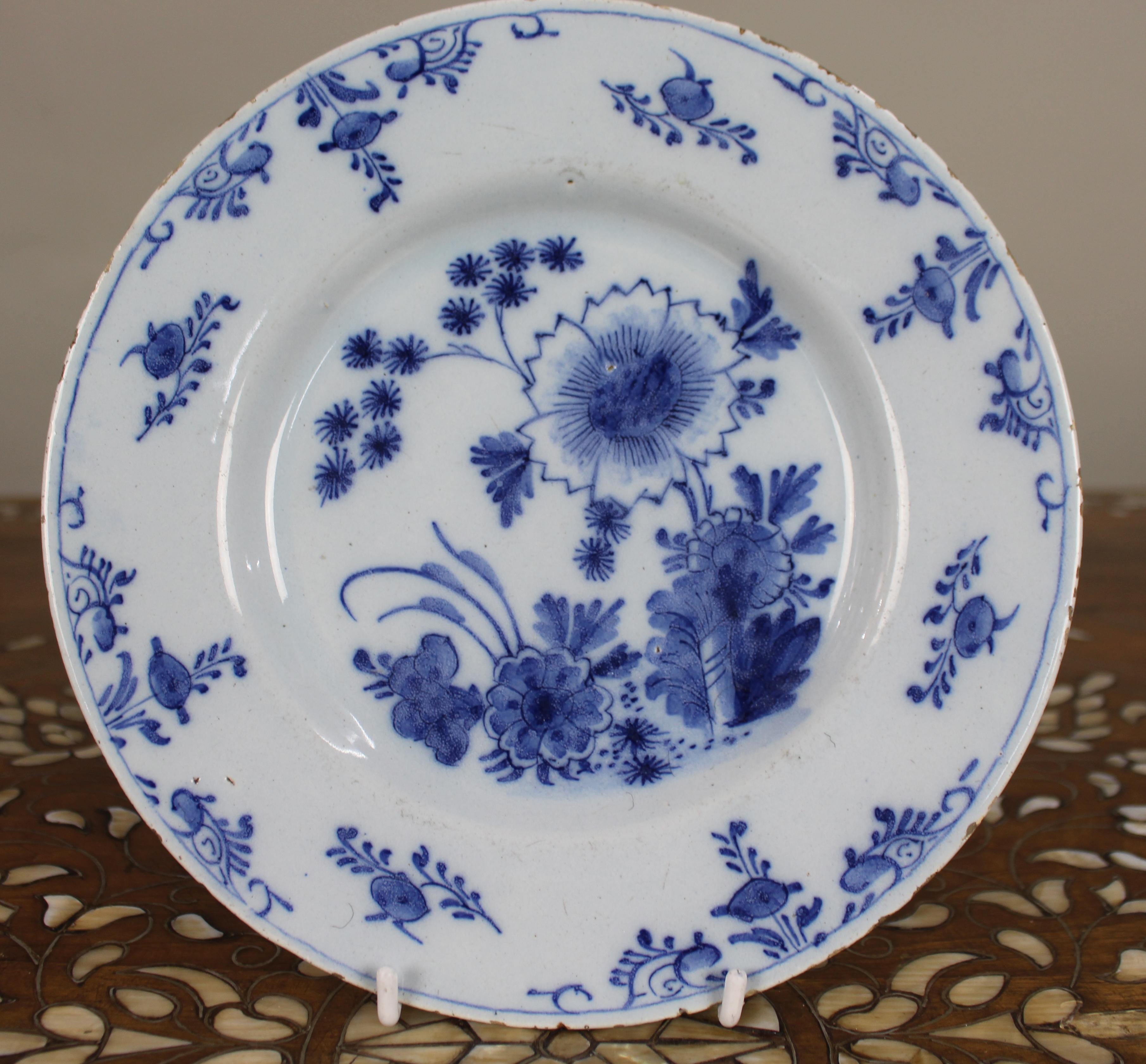 Assiette à fleurs bleu et blanc de Delft du XVIIIe siècle, c.1770

Assiette ancienne en faïence hollandaise, peinte à la main en bleu cobalt sous glaçure, avec un bouquet central de fleurs stylisées, dont un chrysanthème, entouré d'un feuillage et