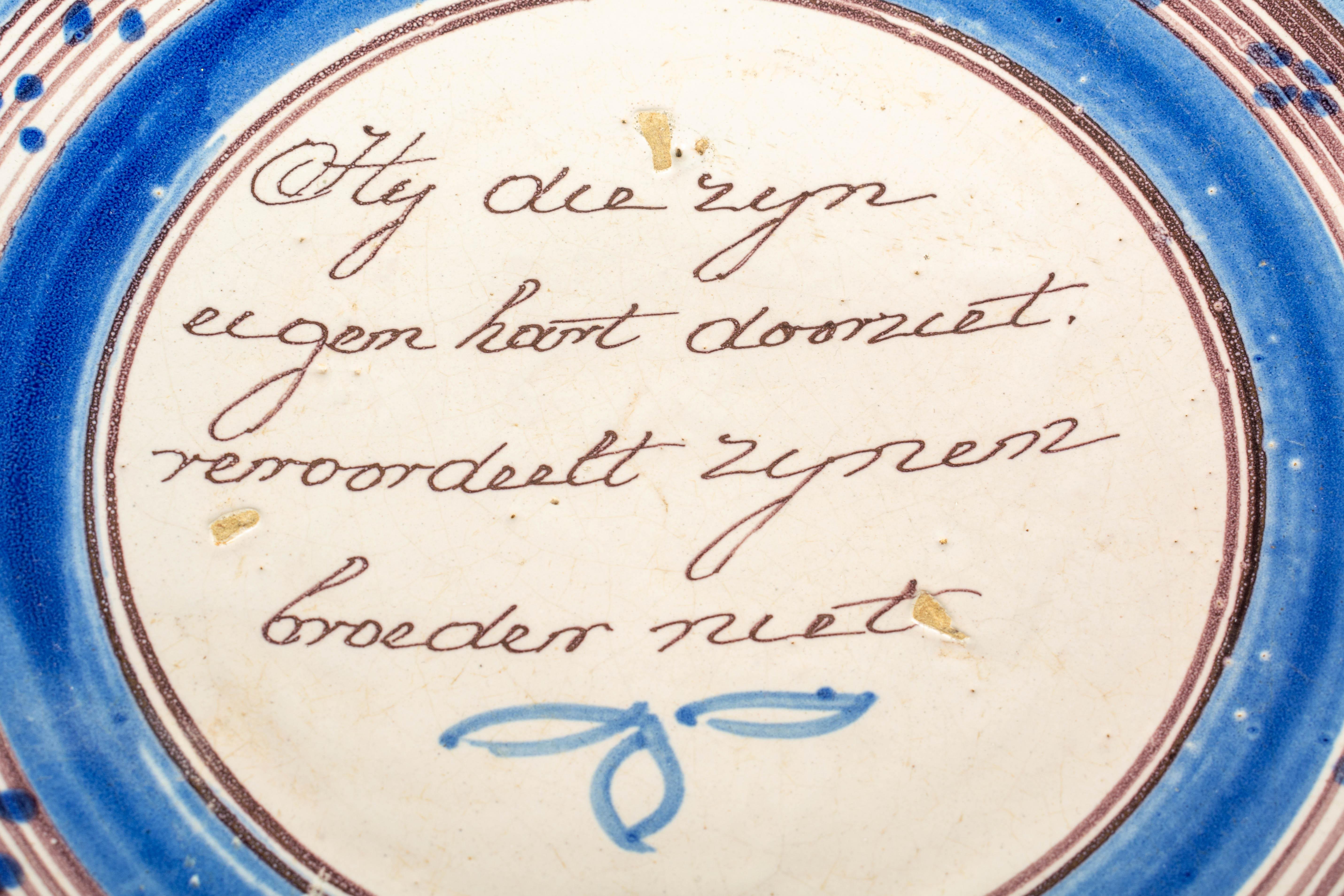 A large late 18th century delft earthenware shallow bowl or dish, decorated in blue, with a handwritten Dutch motto in the center. Rough translation: 
