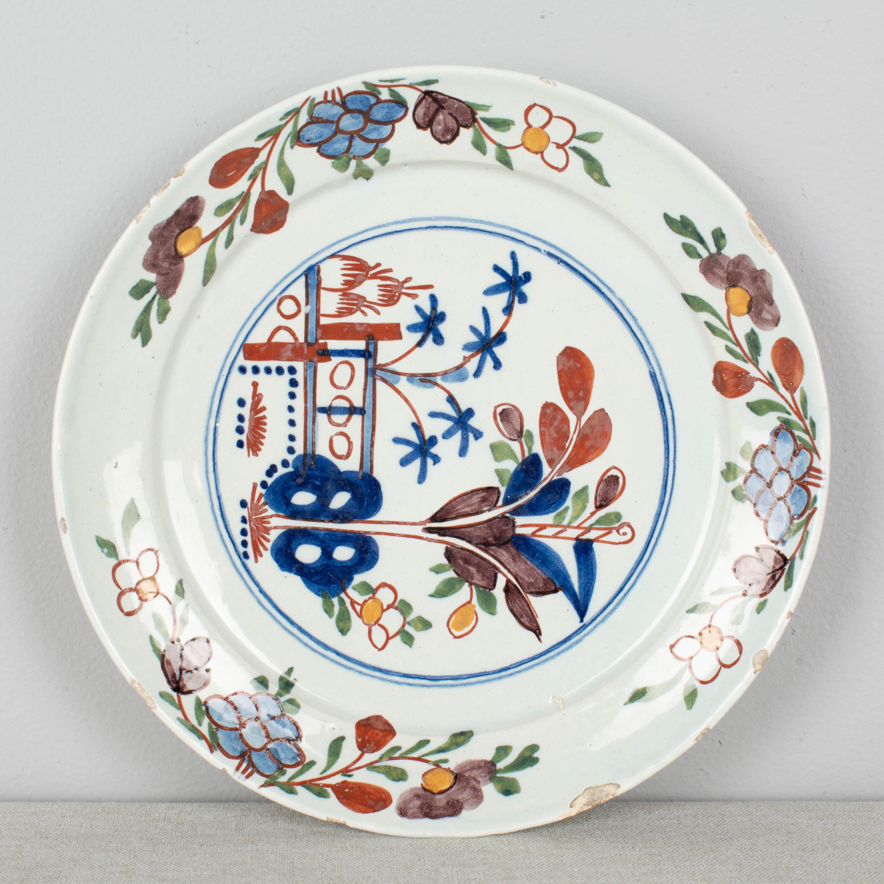 An 18th century Delft ceramic plate, hand-painted in, blue red and green with floral decoration. Several chips to rim.