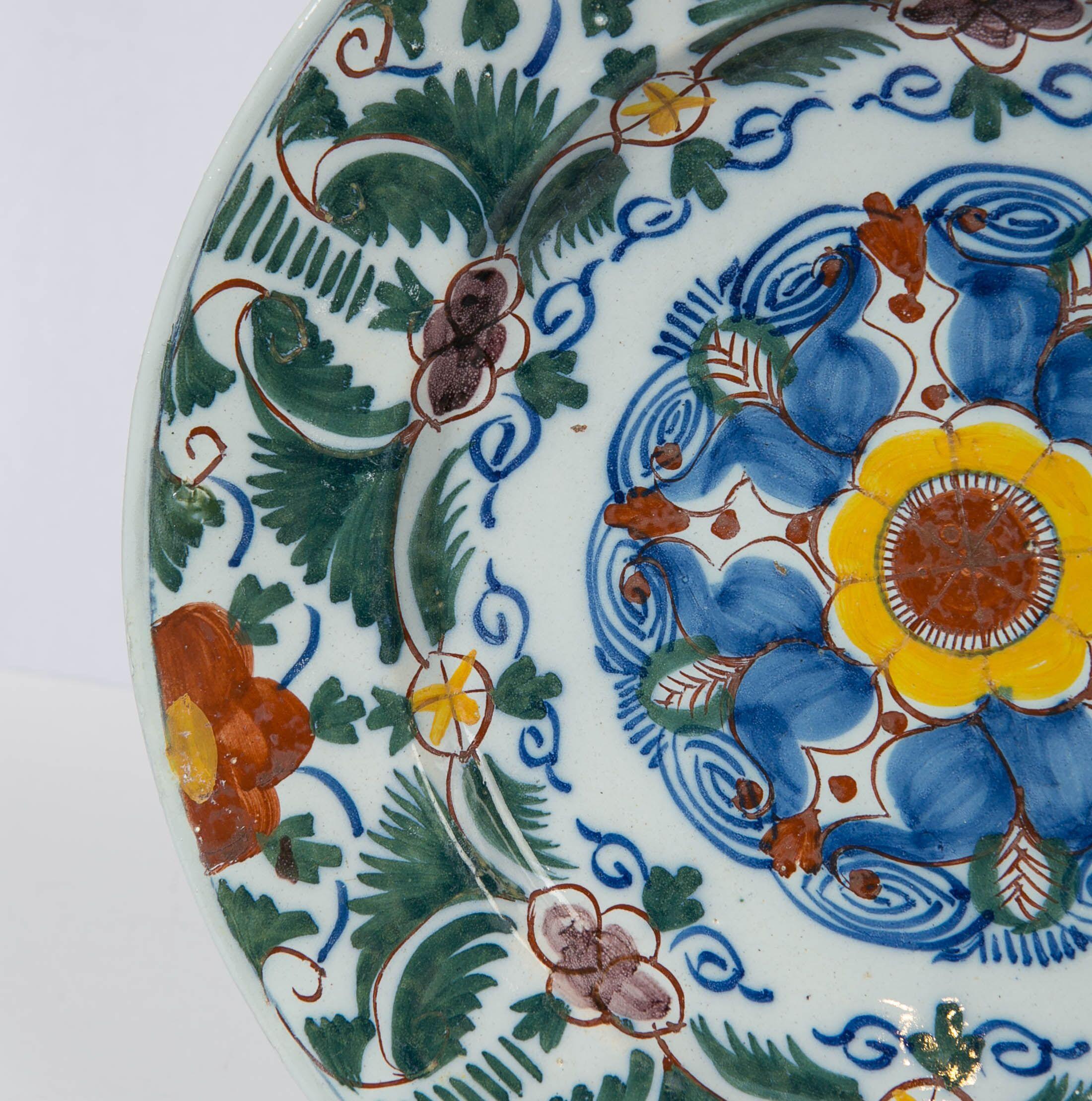 We are proud to offer this 18th-century Dutch Delft charger hand-painted with a burst of polychrome colors: green, blue, orange, and yellow. The colors are painted over the glaze except for the cobalt blue, which is brushed under the glaze. This