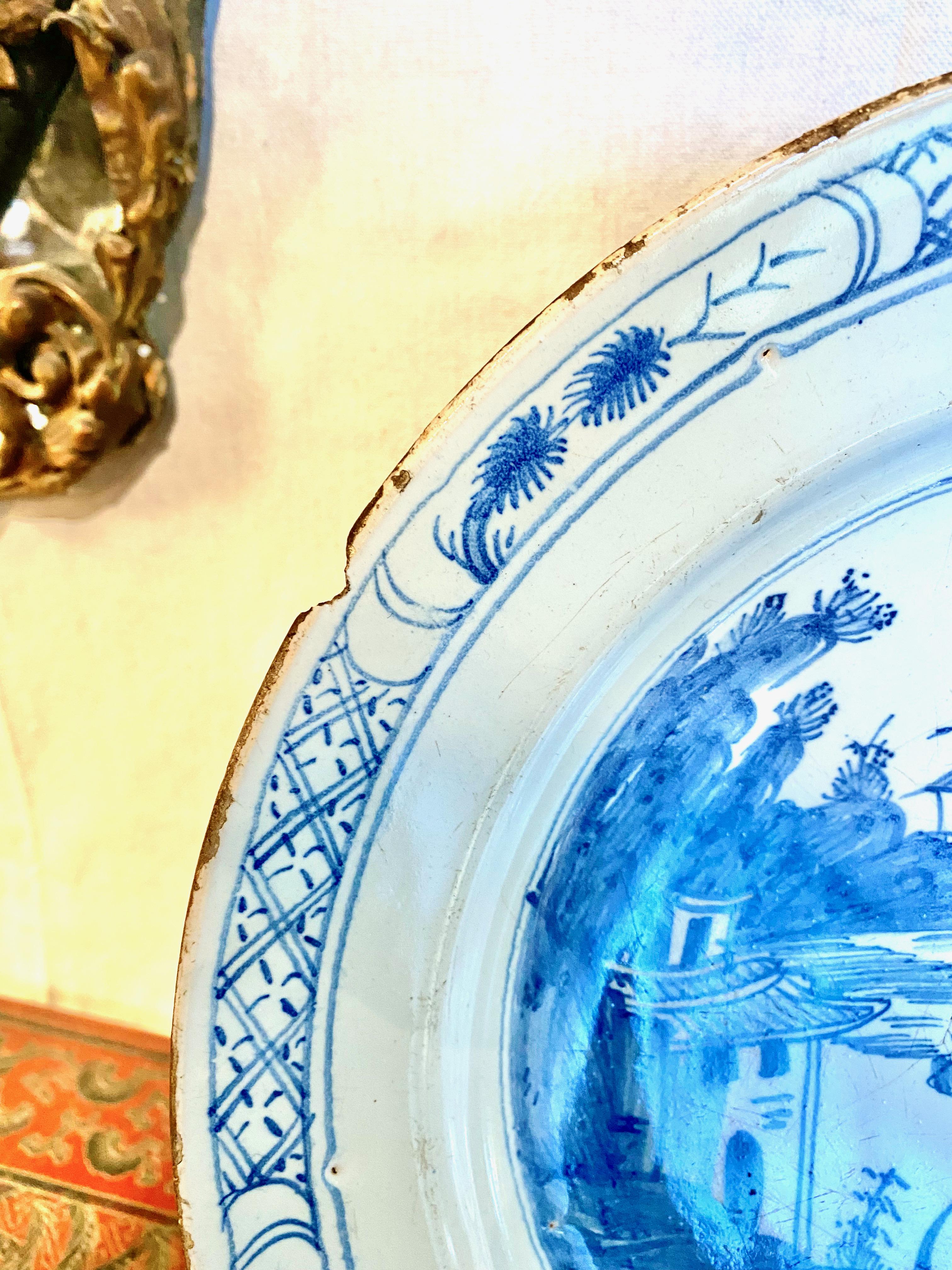 This is a good example of a mid-18th century Delft charger in a chinoiserie hand-painted pattern. The pottery is hand-painted in a traditional blue and white chinoiserie scene featuring a pagoda, lake and willow tree. This charger is a decorative