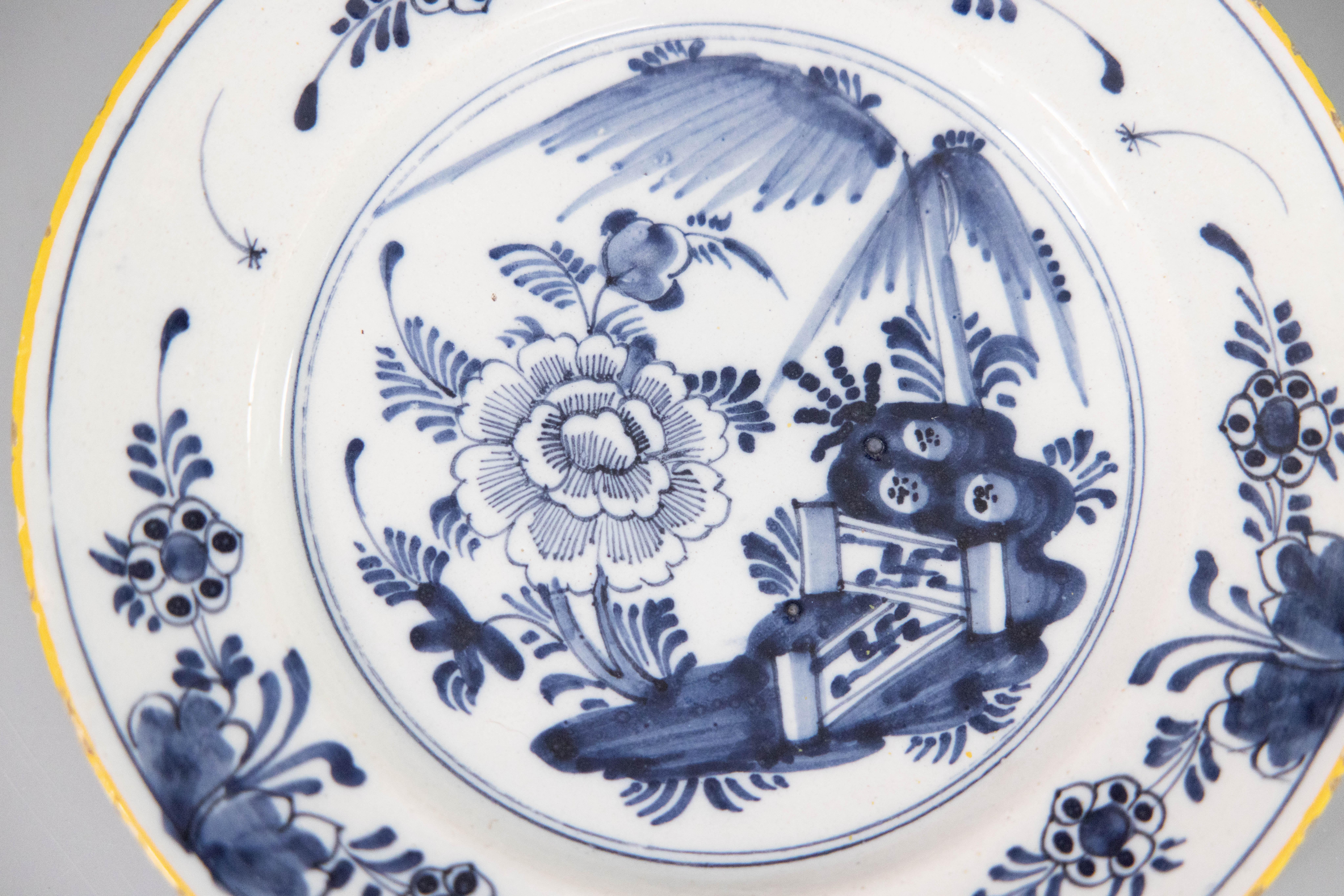 A beautiful antique 18th-Century Dutch Delft faience chinoiserie flower garden plate. This lovely plate has hand painted flowers, fence, and a decorative floral and foliate border in cobalt blue and white with a yellow gold rim. It would be