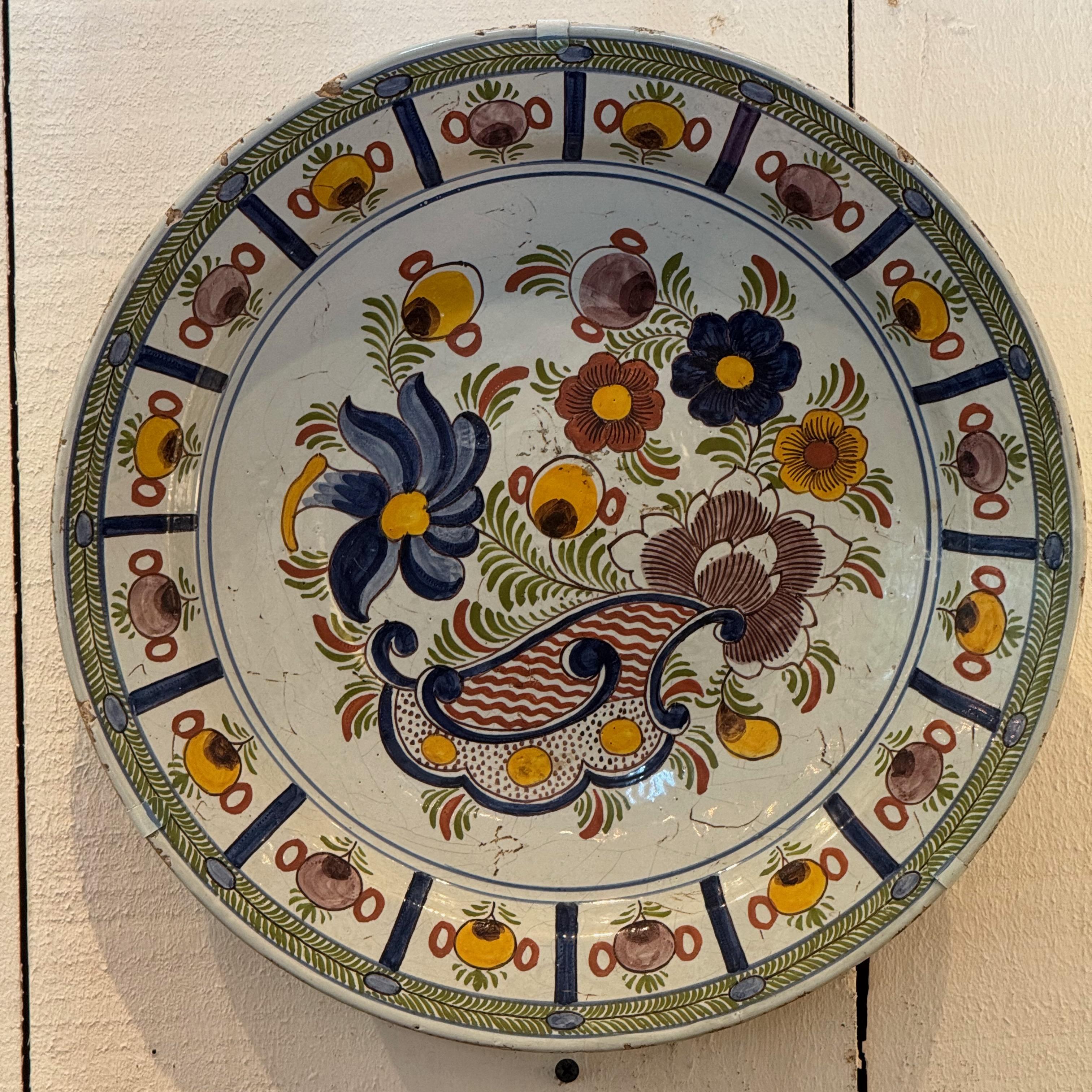Cargador de Delft del siglo XVIII, pintado a mano, con una estilizada voluta central rodeada de vibrantes aerosoles florales. El borde presenta medallones alternados de frutas y flores con un rítmico dibujo geométrico, todo ello en vidriado