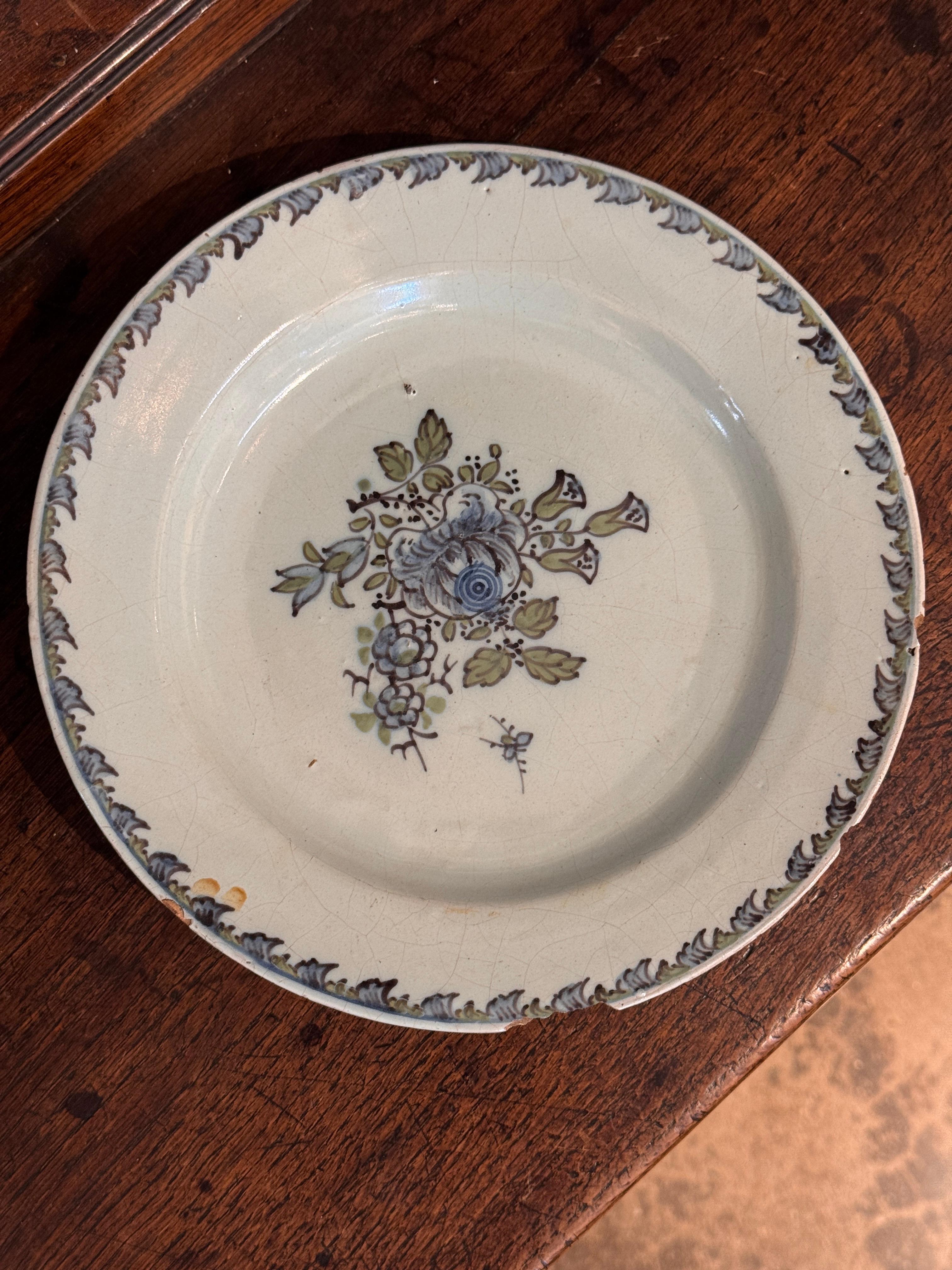 Niederländischer Delft-Teller mit polychromer Bemalung, in der Mitte ein Blumenstrauß in sanften Blau-, Grün- und Mangantönen, umgeben von einer Blattbordüre. Die zinnglasierte Oberfläche weist typische Abnutzungserscheinungen, Glasurverluste und