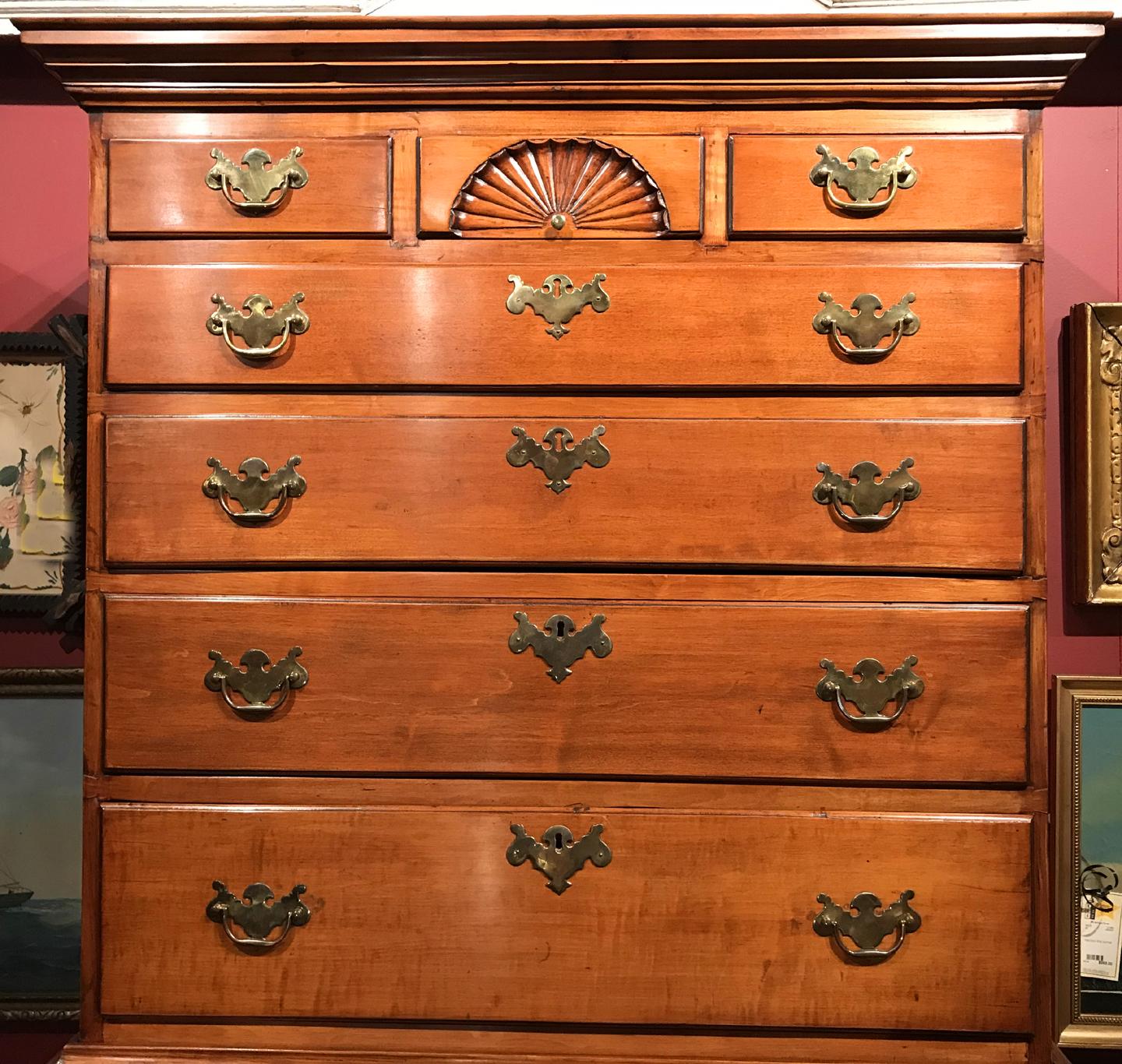 A fine Dunlap School New Hampshire flat top tiger maple two part highboy with a molded cornice surmounting an upper case with a three fitted small drawers over four graduated long drawers, the center fitted drawer featuring a carved radiating fan