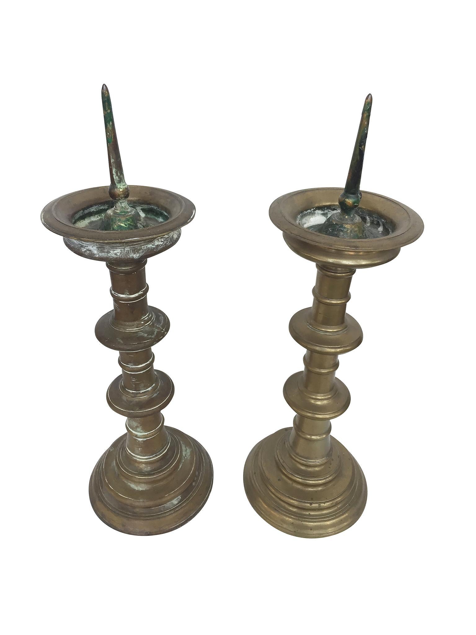 These 18th century Dutch candlesticks are comprised of brass. The drip pan at top is upswept , while the stem is turned and resting on a concentric base.
The patina and coloration differs between the candlesticks, which adds a textured sense of