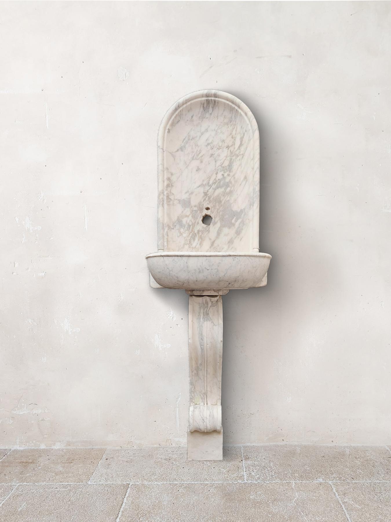 18th century Dutch wall fountain from the hall of a canal house. Made of Carrara marble. Antique wall fountain, with a niche-shaped high back including tap hole, on a curled leg with palmette motif.
(sold without the sample tap that can be seen in