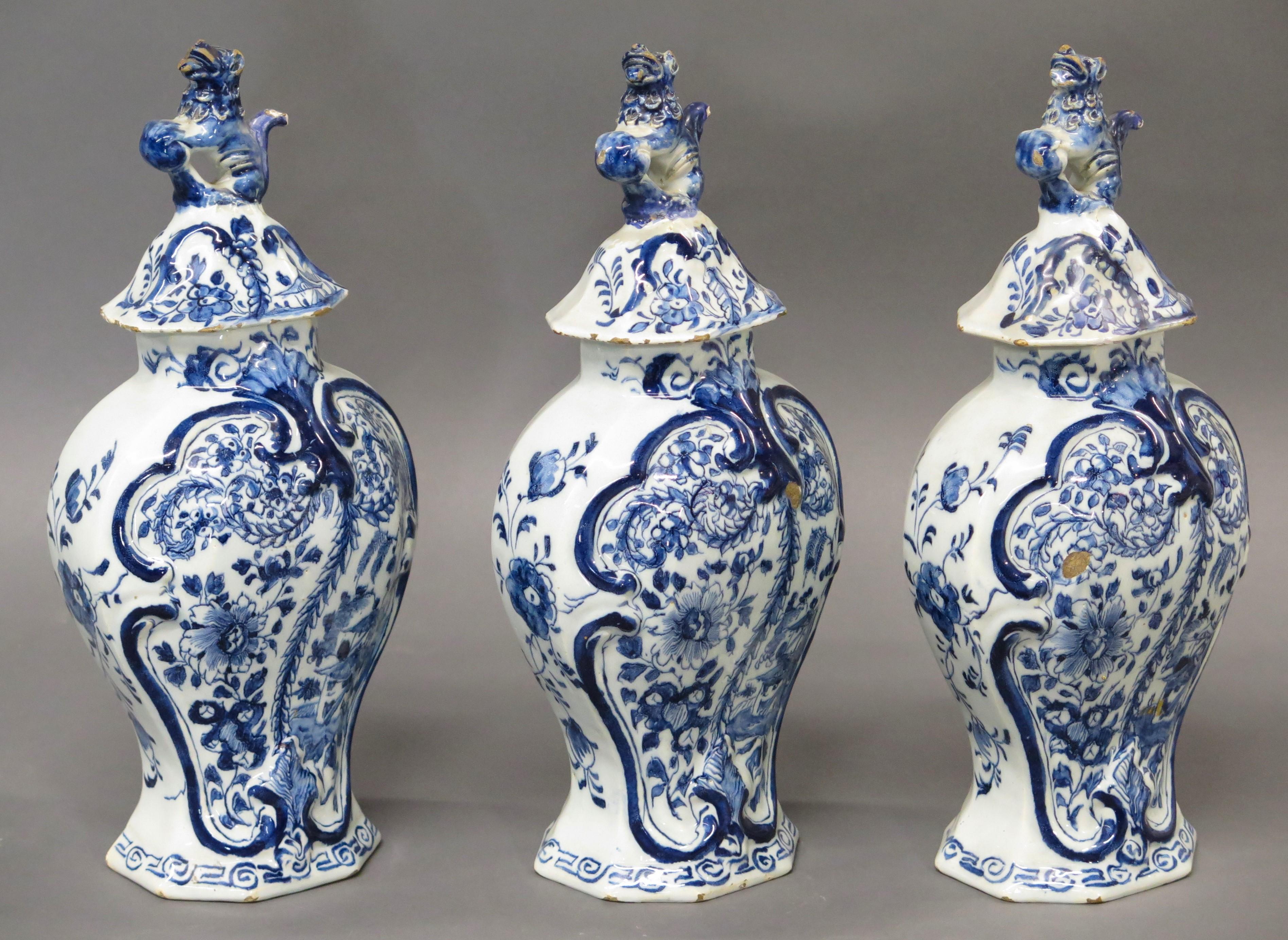 18th Century Dutch delft 3-piece garniture lidded vase set, blue and white with floral panel and relief foliate decorations, with foo dog finials, each vase marked LPK on the base for the 