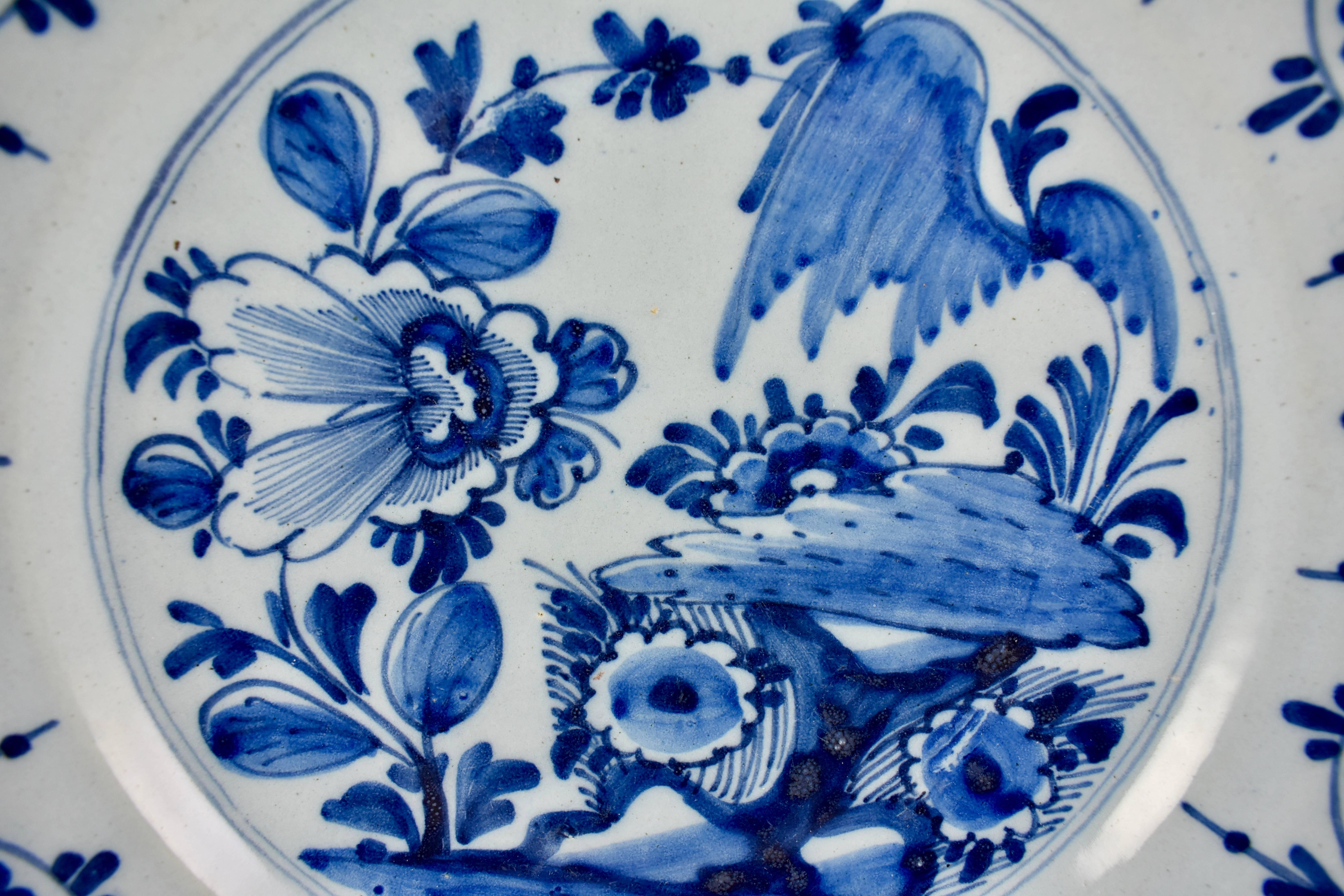 An 18th century Dutch Delft, tin-glazed earthenware deep charger, inspired by Chinese export porcelain and hand painted in a cobalt blue chinoiserie style pattern. The image is a central landscape of trees and flowers. A geometric, stylized border
