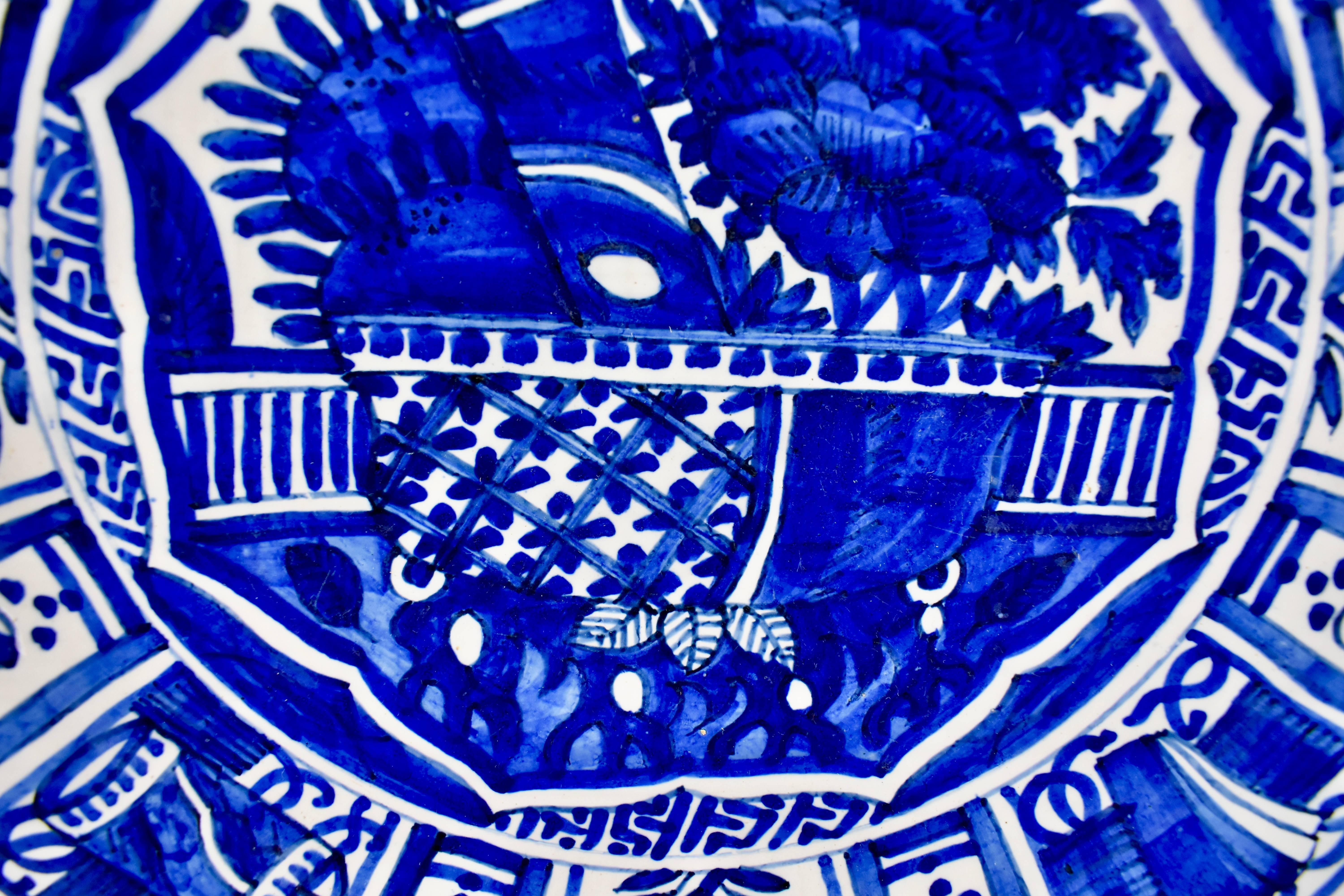 An 18th century Dutch delft, tin-glazed earthenware deep charger, inspired by Chinese export porcelain and hand-painted in a heavy cobalt blue geometric and floral pattern. A stylized border of a daisy like flower alternating with a geometric