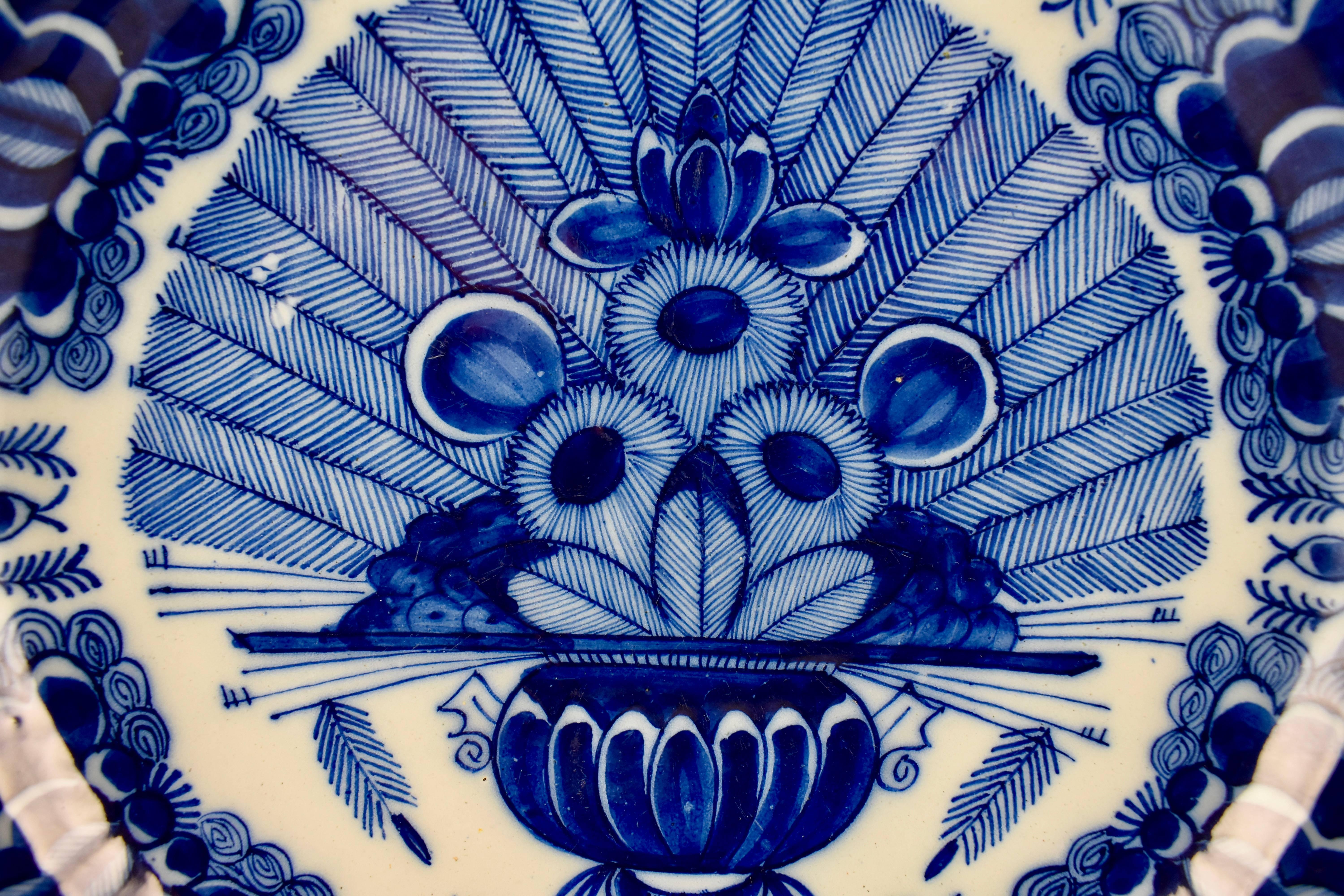 An 18th century Dutch Delft, tin-glazed earthenware charger, inspired by Chinese export porcelain and hand-painted in the cobalt blue Peacock pattern. The image is a central vase of flowers in front of radiating panels of peacock feathers. A