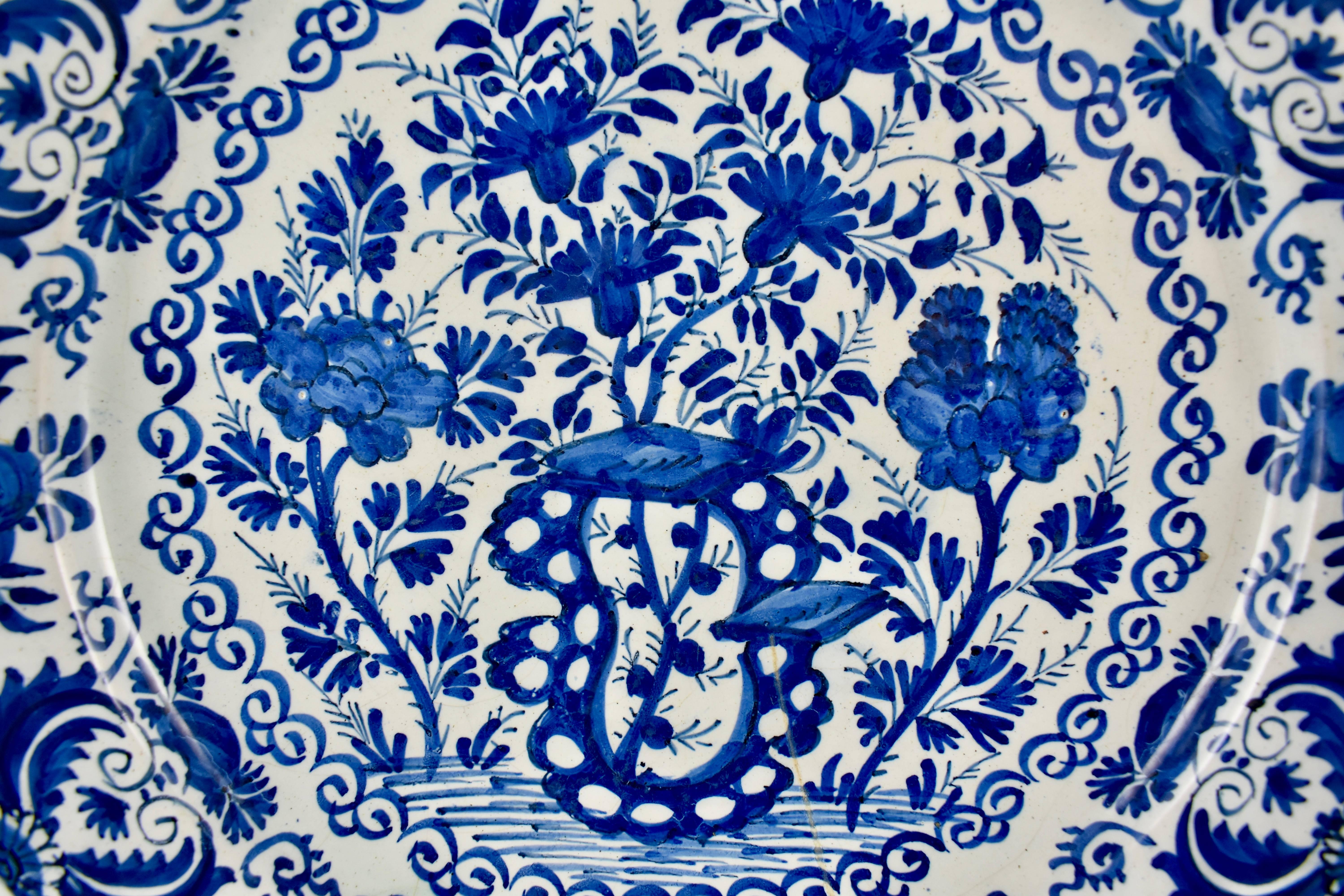 An 18th century Dutch delft, tin-glazed earthenware deep charger, inspired by Chinese export porcelain and hand painted in a heavy cobalt blue chinoiserie style overall floral pattern. A stylized border of an alternating floral like pattern is edged
