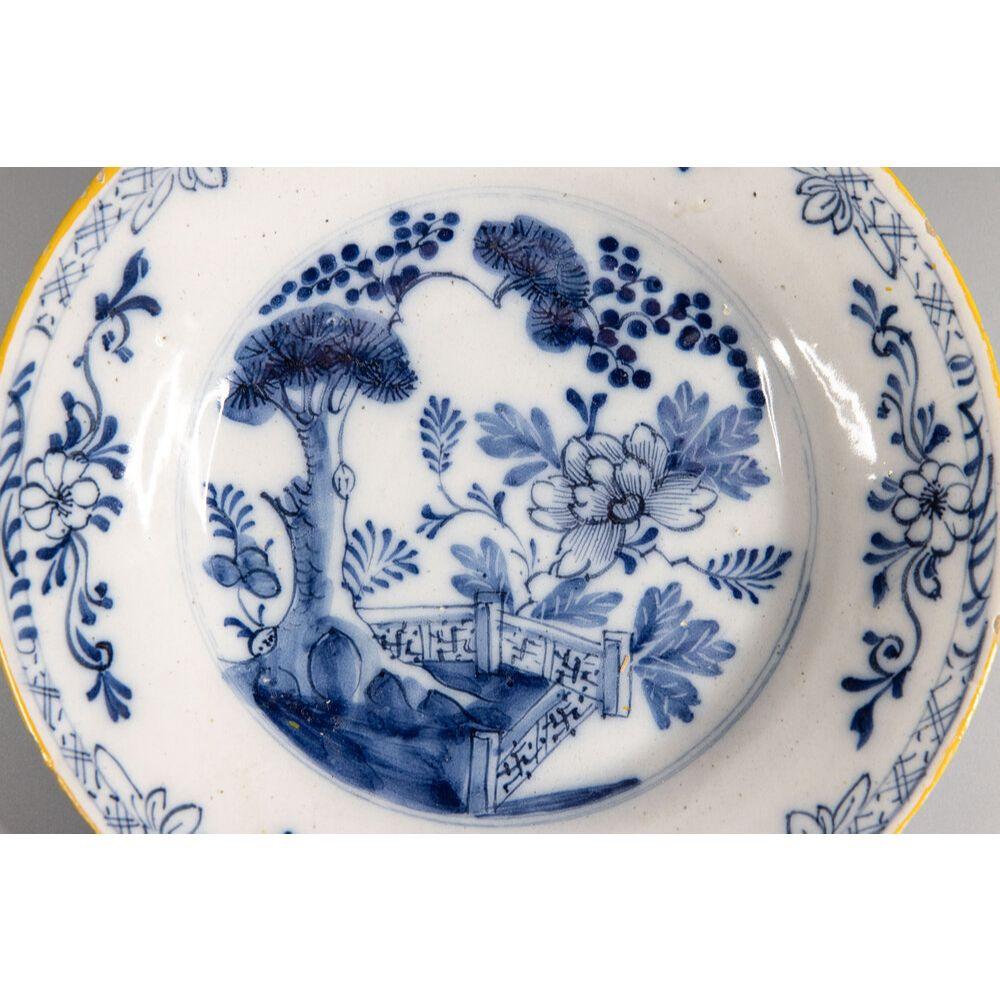 A beautiful antique 18th-Century Dutch Delft faience chinoiserie plate. This lovely plate has a hand painted flower, fence, tree, and floral border in cobalt blue and white with a yellow gold rim. It would be wonderful added to a collection,