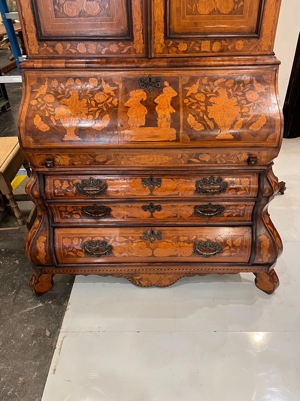 An exquisite 18th-century Dutch marquetry secretary, adorned with meticulous inlay work depicting urns, vines, and floral motifs. Its double-door top cabinet adds grandeur, while the desk boasts numerous compartments and cubby storage drawers,