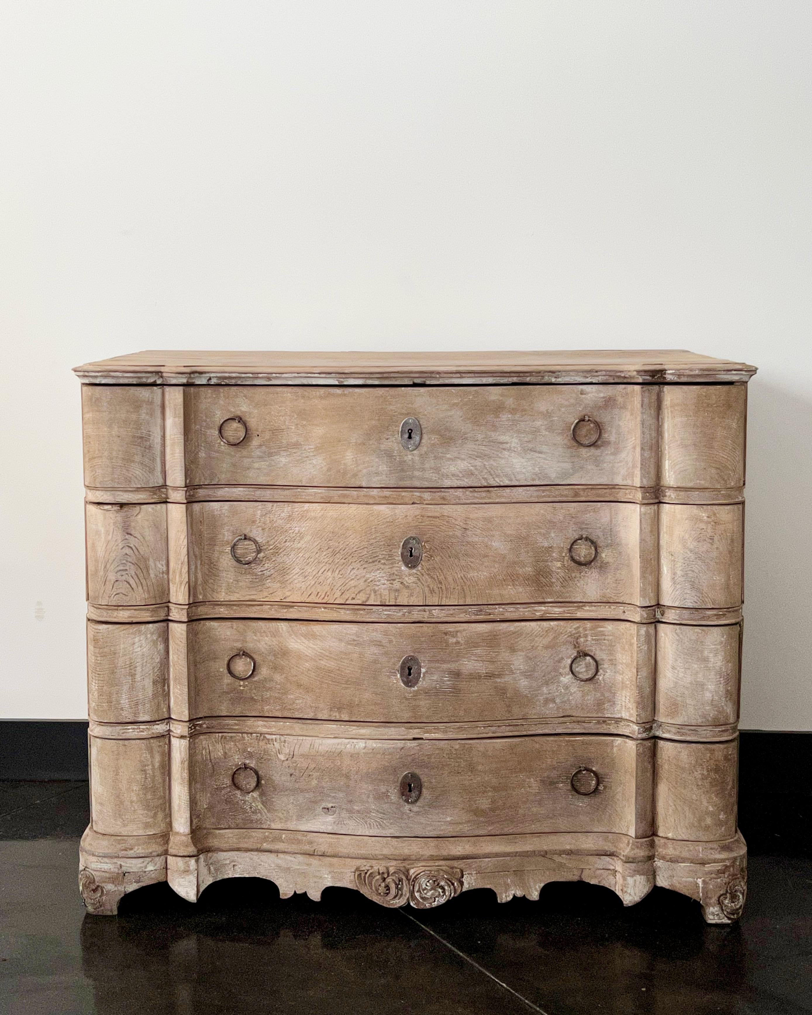 18th century four drawers Dutch chest in richly carved, bleached oak with curvaceous serpentine drawer fronts, shaped top, handsome original large iron handles on the side panels and beautifully carved apron and feet.