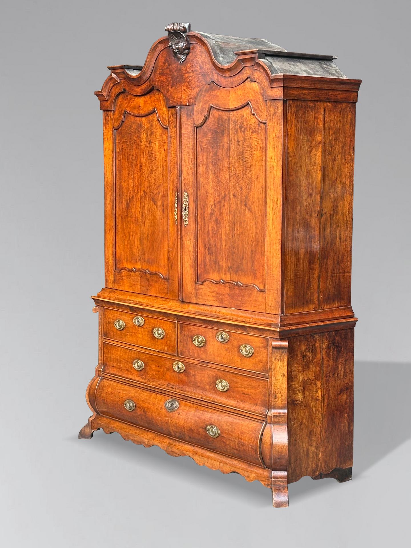 Ce superbe meuble en trois parties en noyer rococo hollandais du milieu du XVIIIe siècle est construit sur un coffre à bombes. Il présente un fronton arqué magnifiquement sculpté, orné d'une crête en forme de coquille et surmonté d'une corniche
