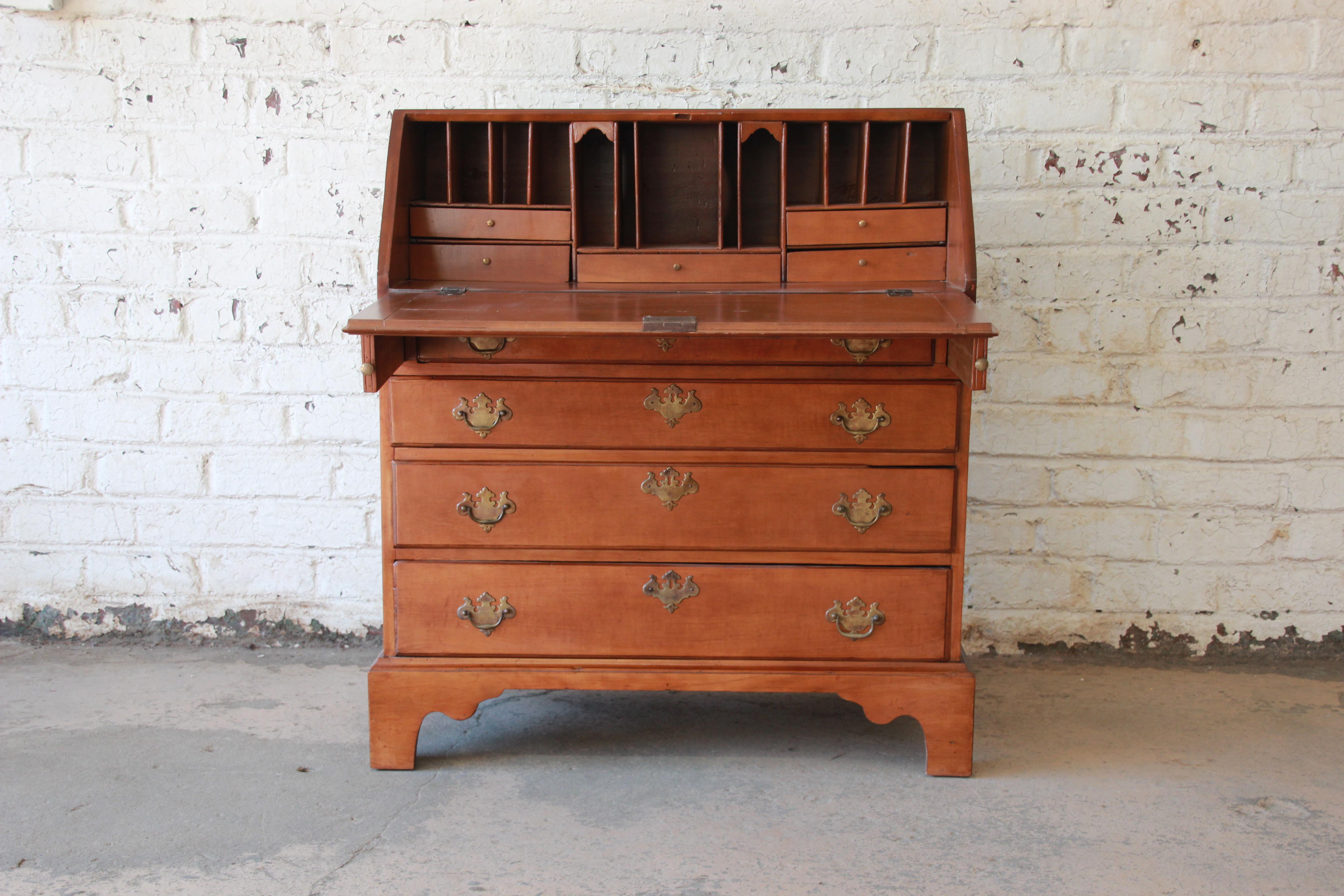 A stunning 18th century early American cherrywood drop-front secretary desk. The desk features solid wood construction, with gorgeous cherry wood grain. It offers ample room for storage, with five drawers and several mail slots behind the drop-front