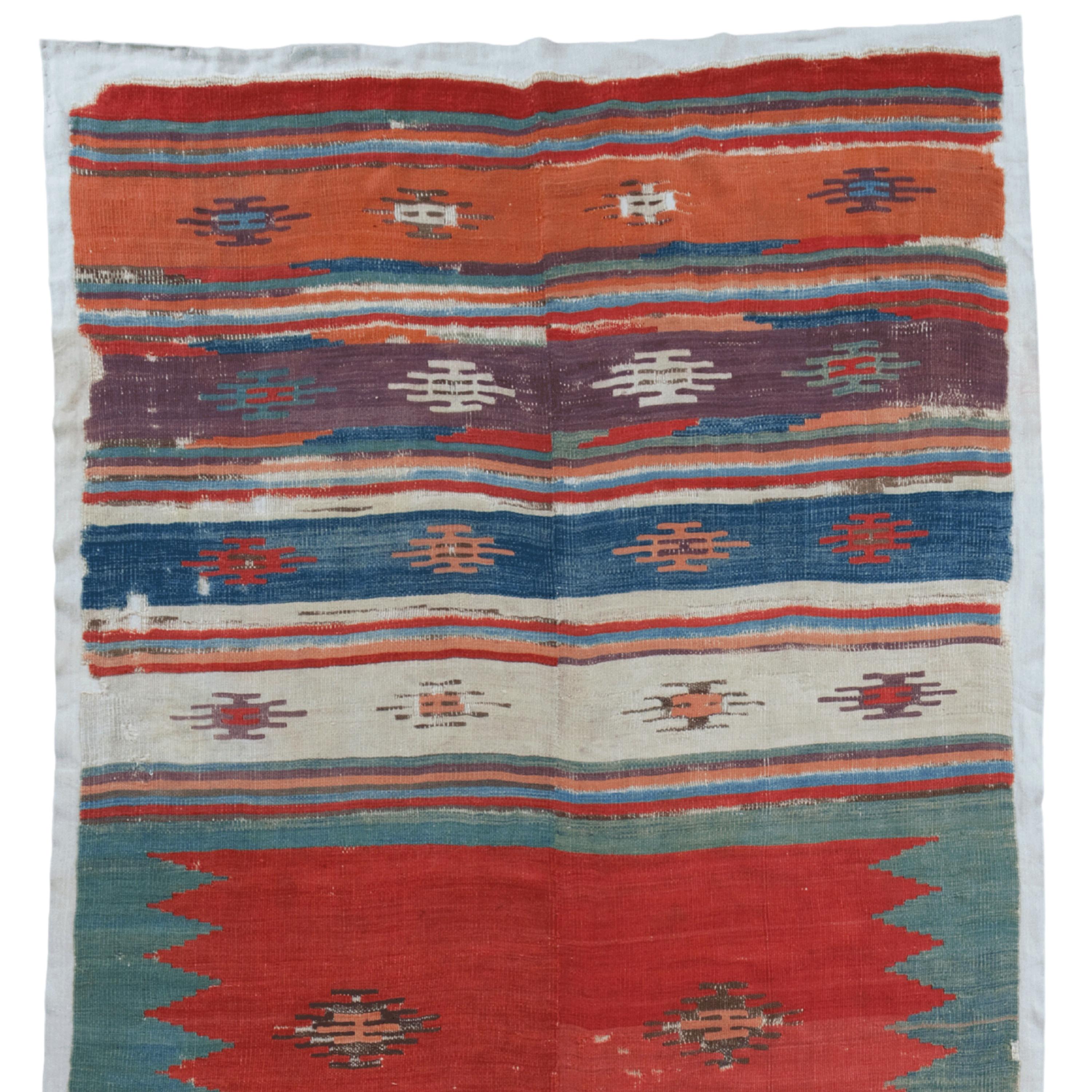 This 18th-century antique Sivas rug features a series of horizontal bands decorated with traditional motifs. A vibrant red central area is surrounded by bands of blue, white and earth tones. Each band contains geometric patterns and stylized floral