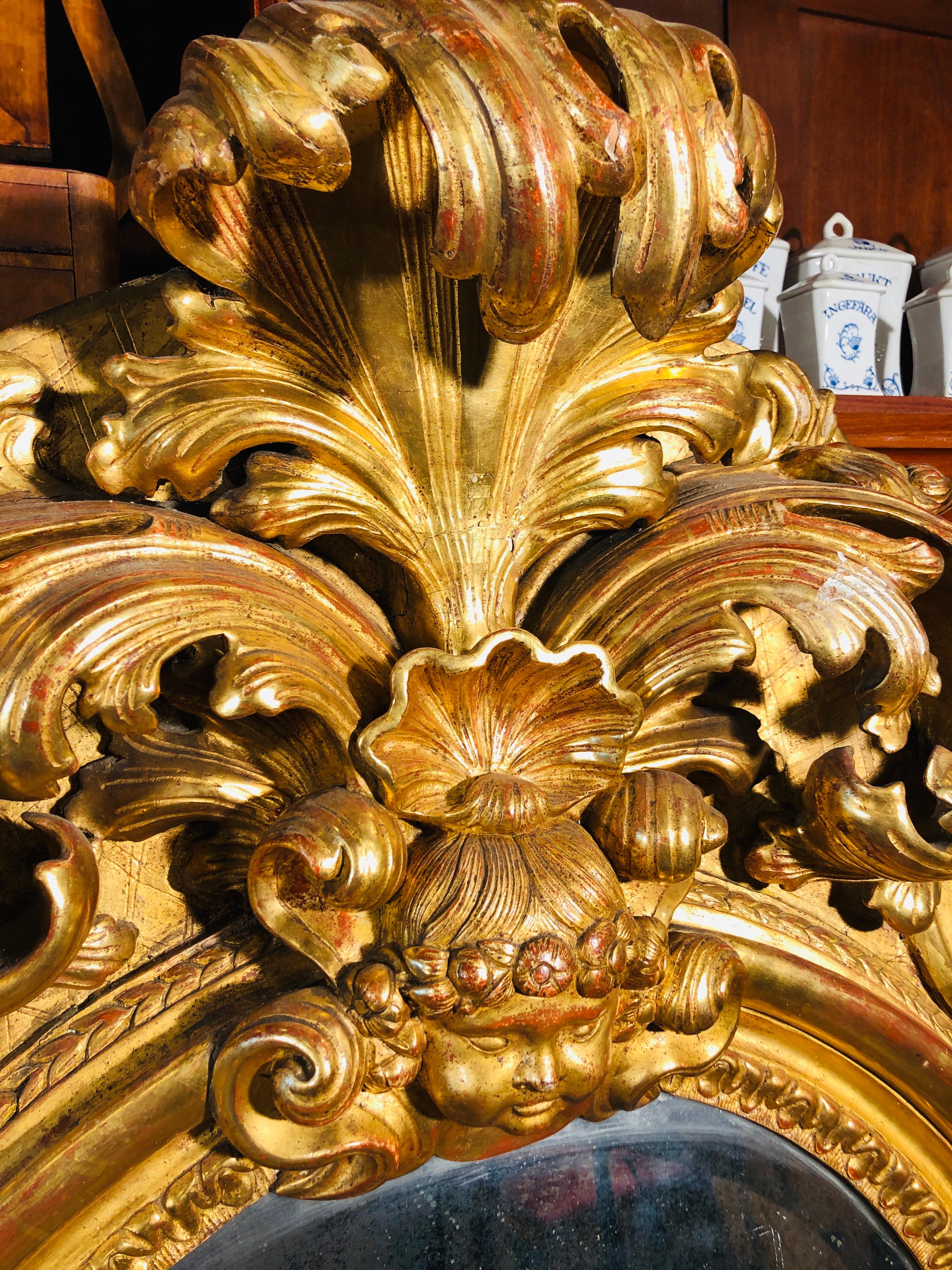 Specchio in legno dorato, di origine romana, centro Italia, periodo Impero in stile Luigi XV, finemente intagliato con bambocci, maschere e motivi floreali, oggetto di grande qualità ed eleganza; specchi di questa fattura venivano commissionati da
