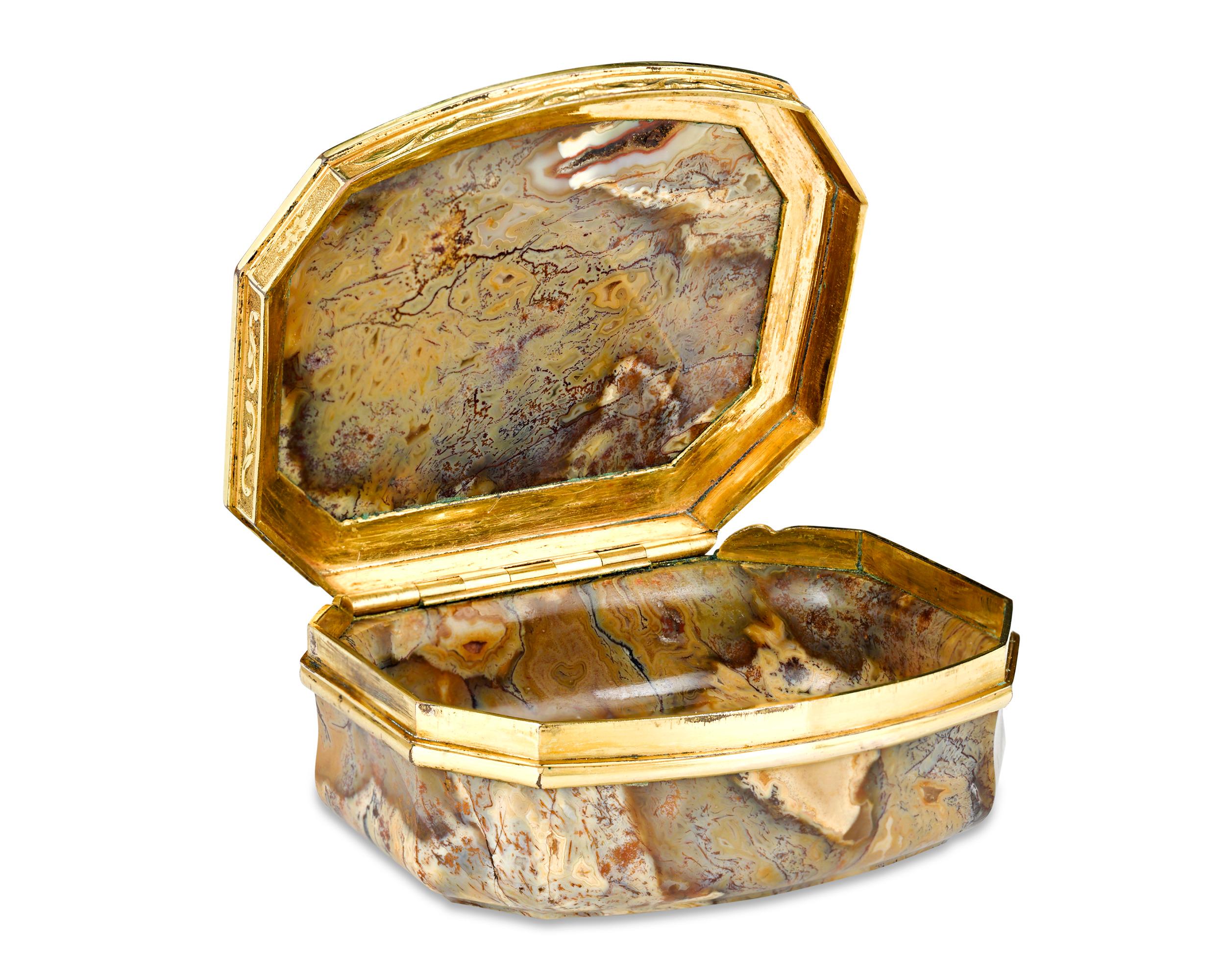 Trimmed in elegant yellow gold is this polished English agate snuff box. Distinguished by the dynamic patterning of the agate, the exquisite vessel is the finely chiseled 10-Karat gold foliage, which provides a beautiful contrast. Symbols of luxury