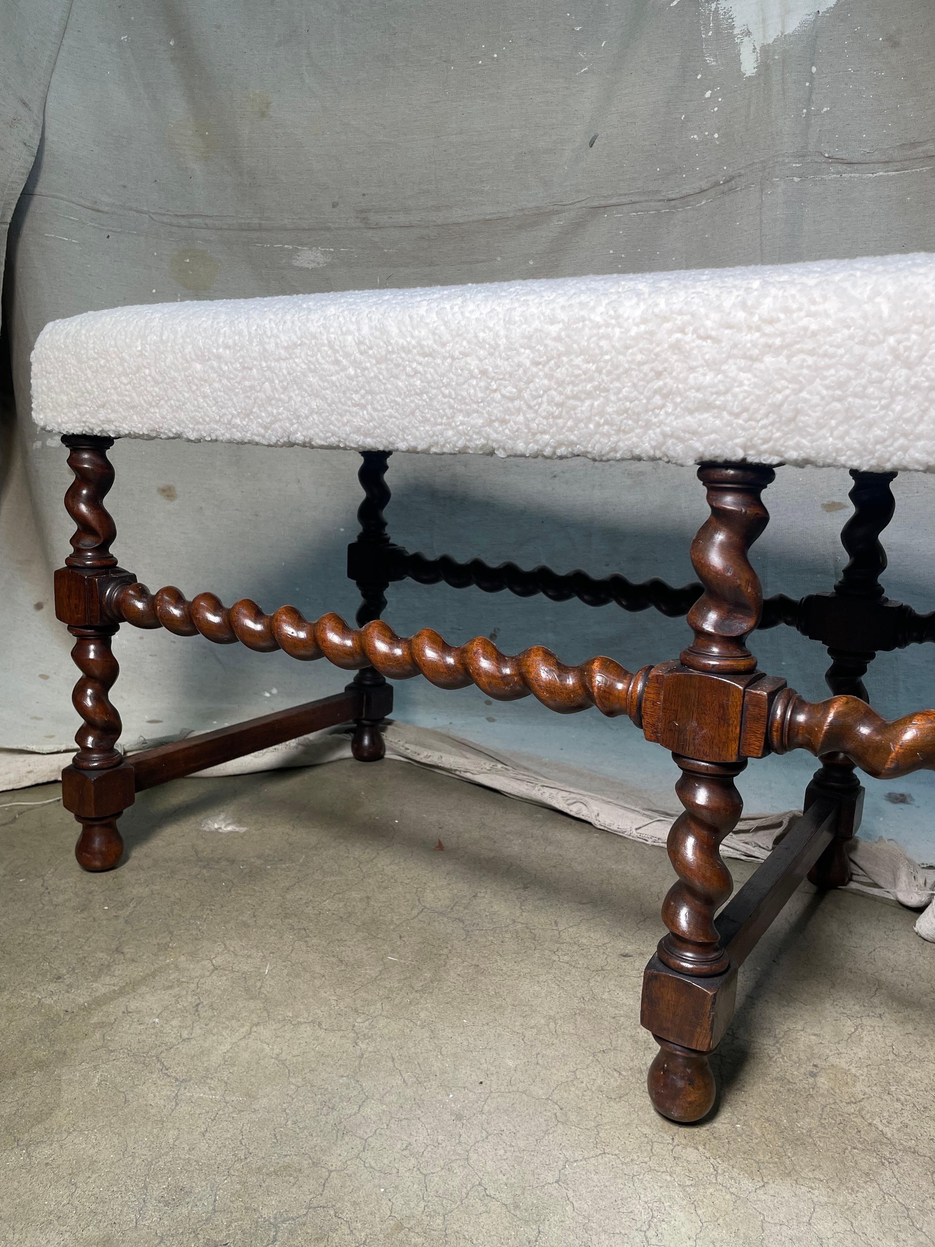 English Mid Century Modern wooden bench from the 18th century with barley twist base and white boucle upholstery. This classy, barley twist wooden bench oozes timeless elegance. This piece is characterized by its base which is not only for
