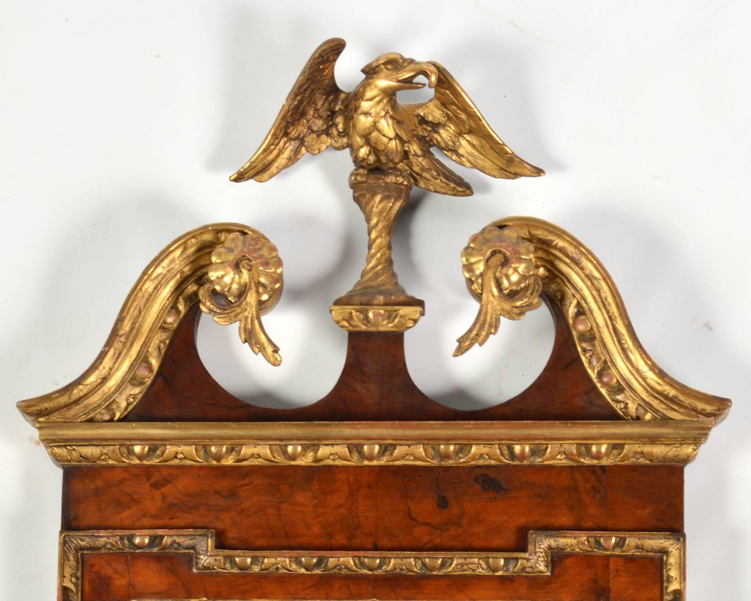 This fine and unusually wall mirror features a carved scrolled giltwood pediment surmounted by a likewise carved and gilded eagle. The sides are aorned by carved giltwood open leafwork applied to the baroque style border surrounding the looking