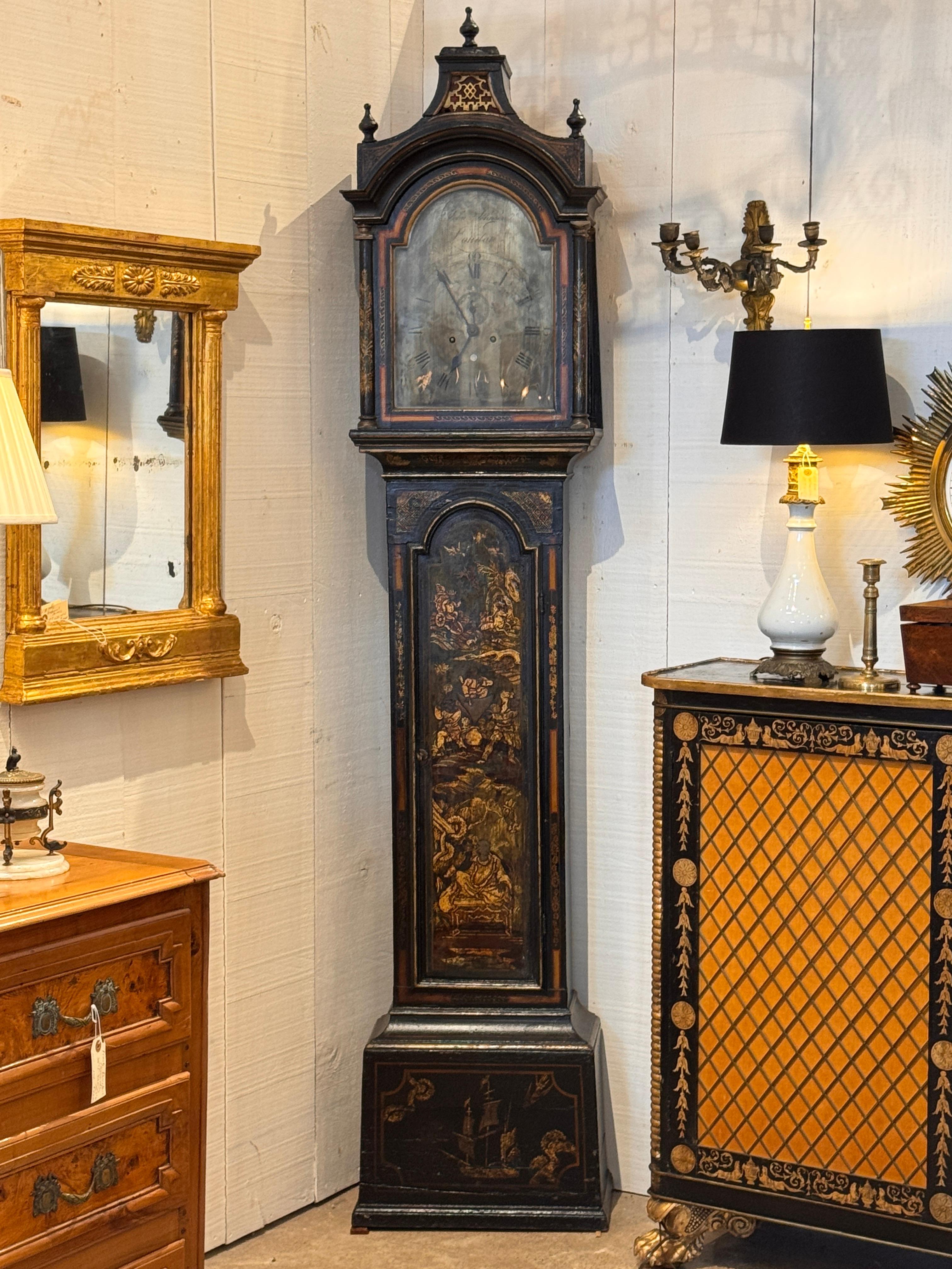 An 18th century English longcase clock with chinoiserie decoration on a black lacquer ground, featuring gilt figures, pagodas, and landscape motifs throughout the case. The arched hood with finials and pierced fretwork encloses a silvered dial with