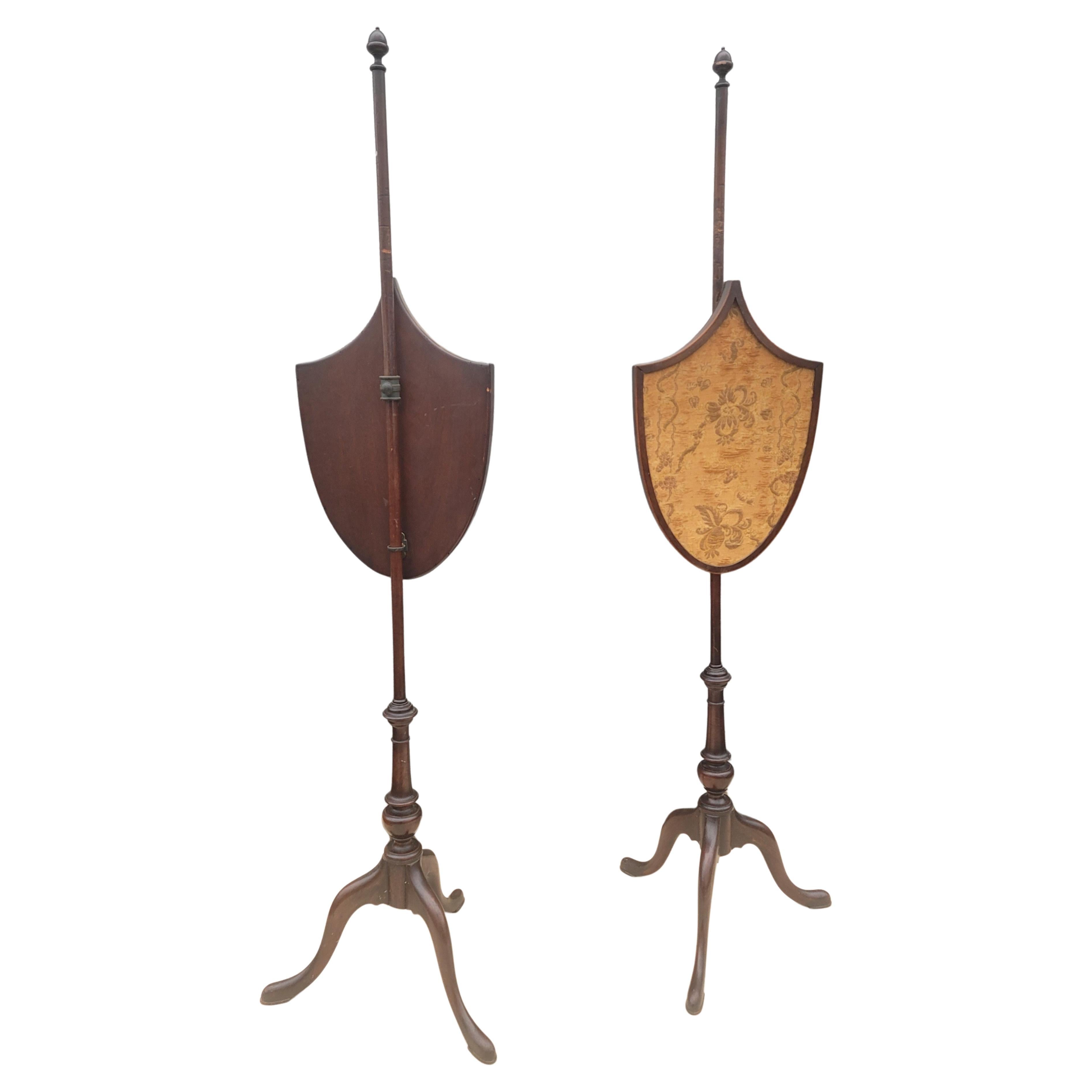 A pair of English Chippendale mahogany shield back with original needlepoint work pole screens with a urn finial , telescopic turned bulbous shaft, and terminating on tripod snake feet. Adjustable height screen panels mid-18th century.