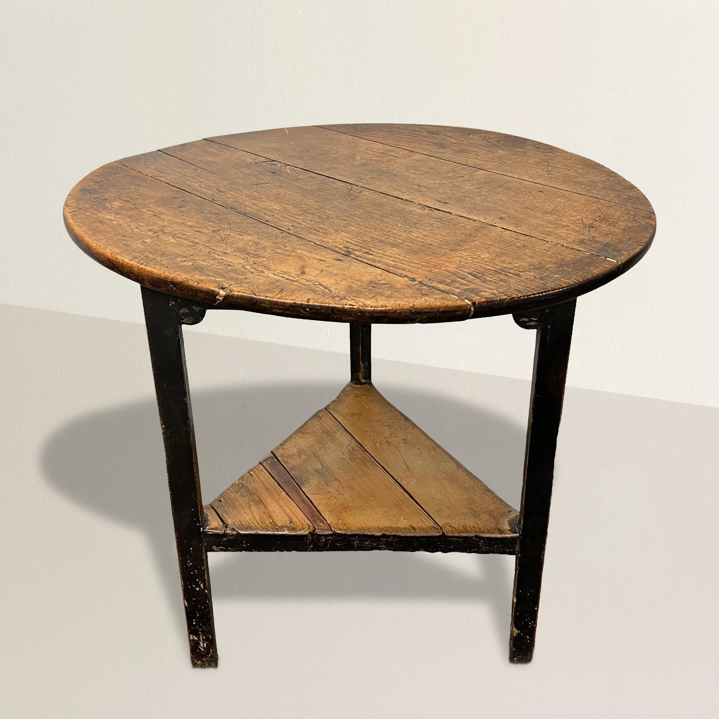 Standing as a testament to 18th-century English craftsmanship, this exceptional elmwood cricket table is a captivating piece of furniture. Its round top and shelf boasts a patina that tells the tale of years gone by. Supported by three elegantly