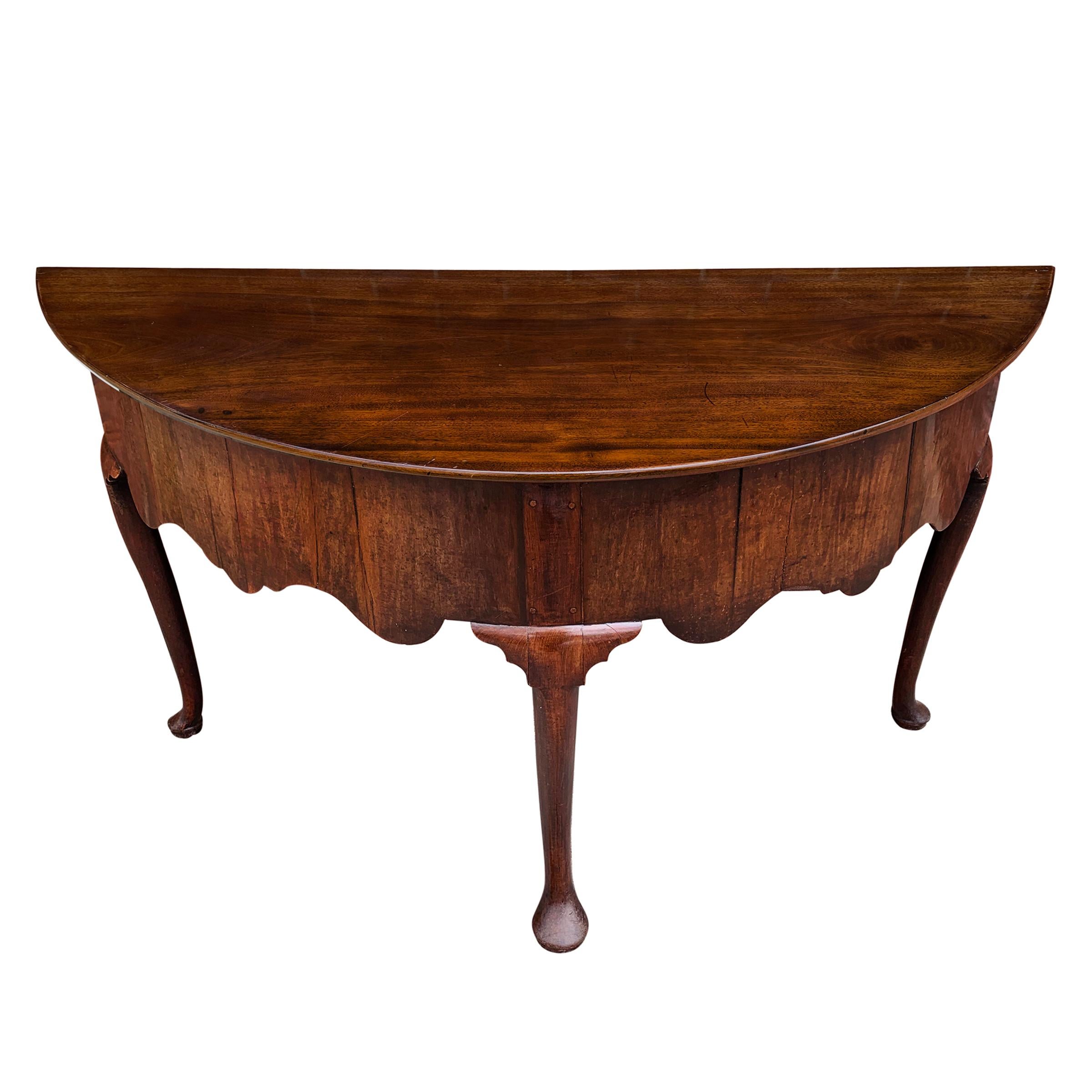 An incredible 18th century English Queen Anne style mahogany demilune table with an exaggerated wide scalloped apron and three cabriole legs ending in wide pad feet, the center foot being larger than the other two. The top is of one piece of wood