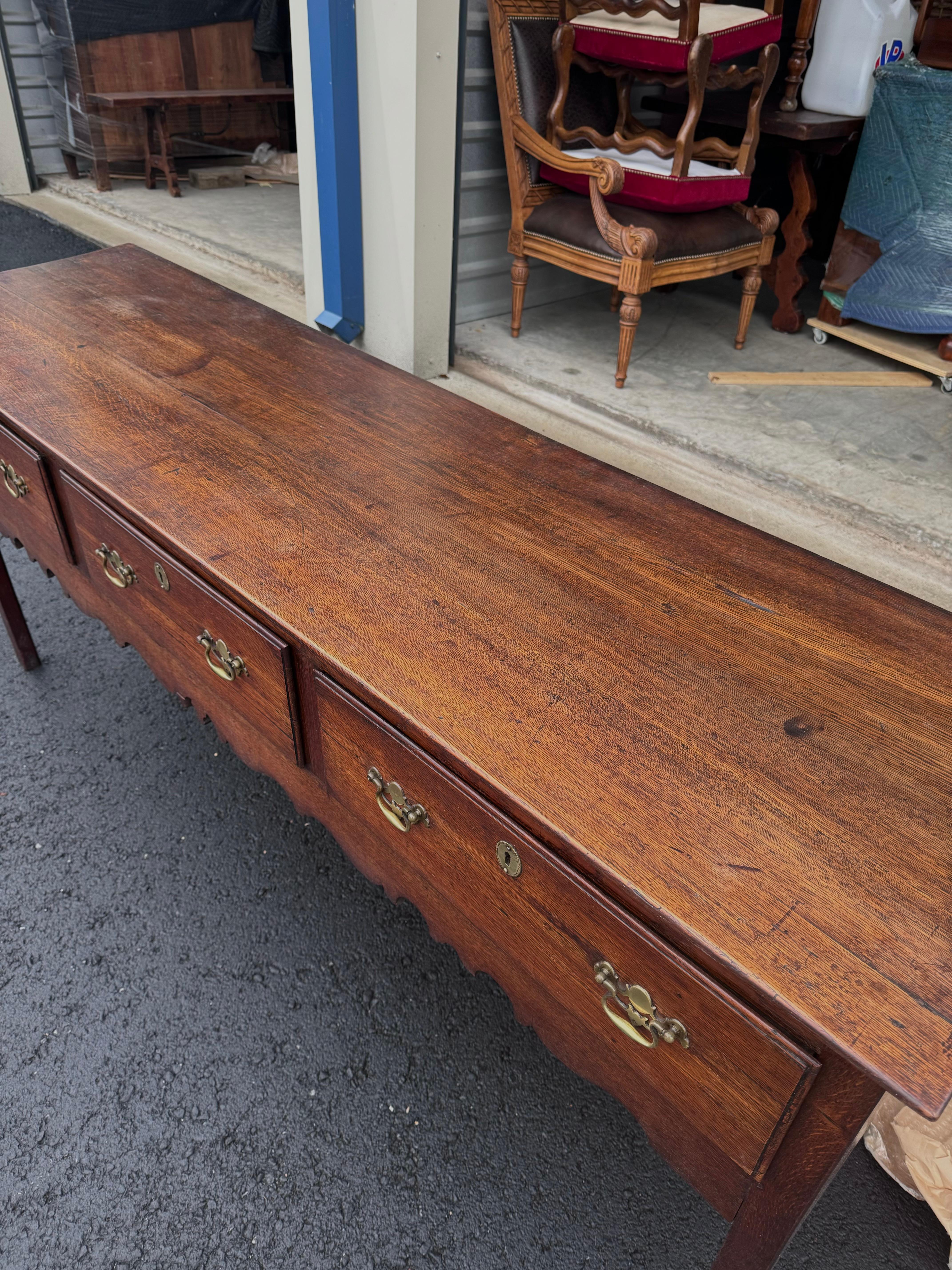 Own a piece of history with this 18th Century English Welsh Dresser Base. Crafted with timeless charm, this antique dresser exudes rustic simplicity. The sturdy wooden construction and warm patina and brass pulls tells a story of centuries gone by.