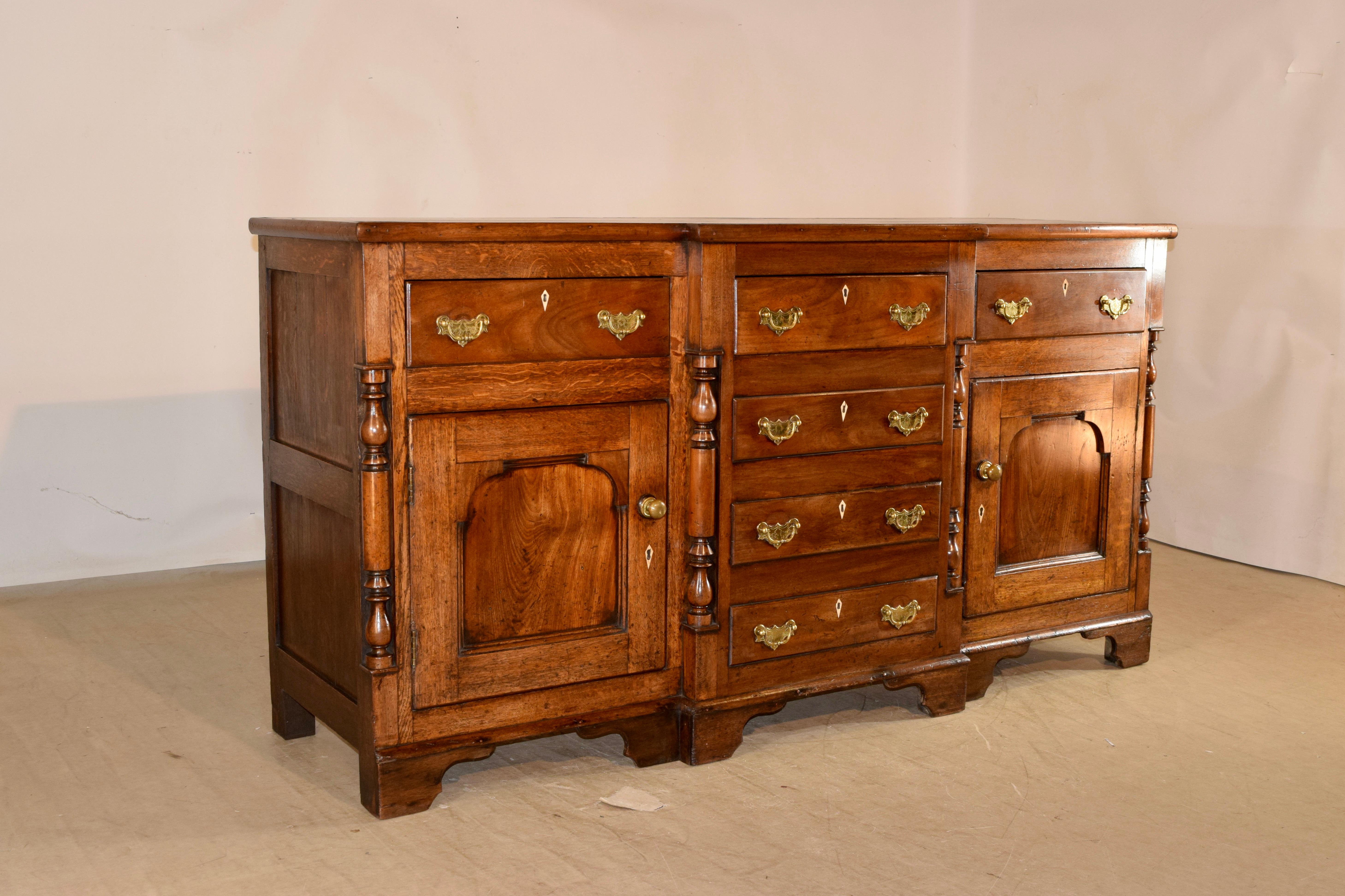 18th Century oak and elm dresser base from England. The top is made from three planks with a blocked front, following down to paneled sides and a block front case. The central section of which contains four drawers flanked with two hand turned