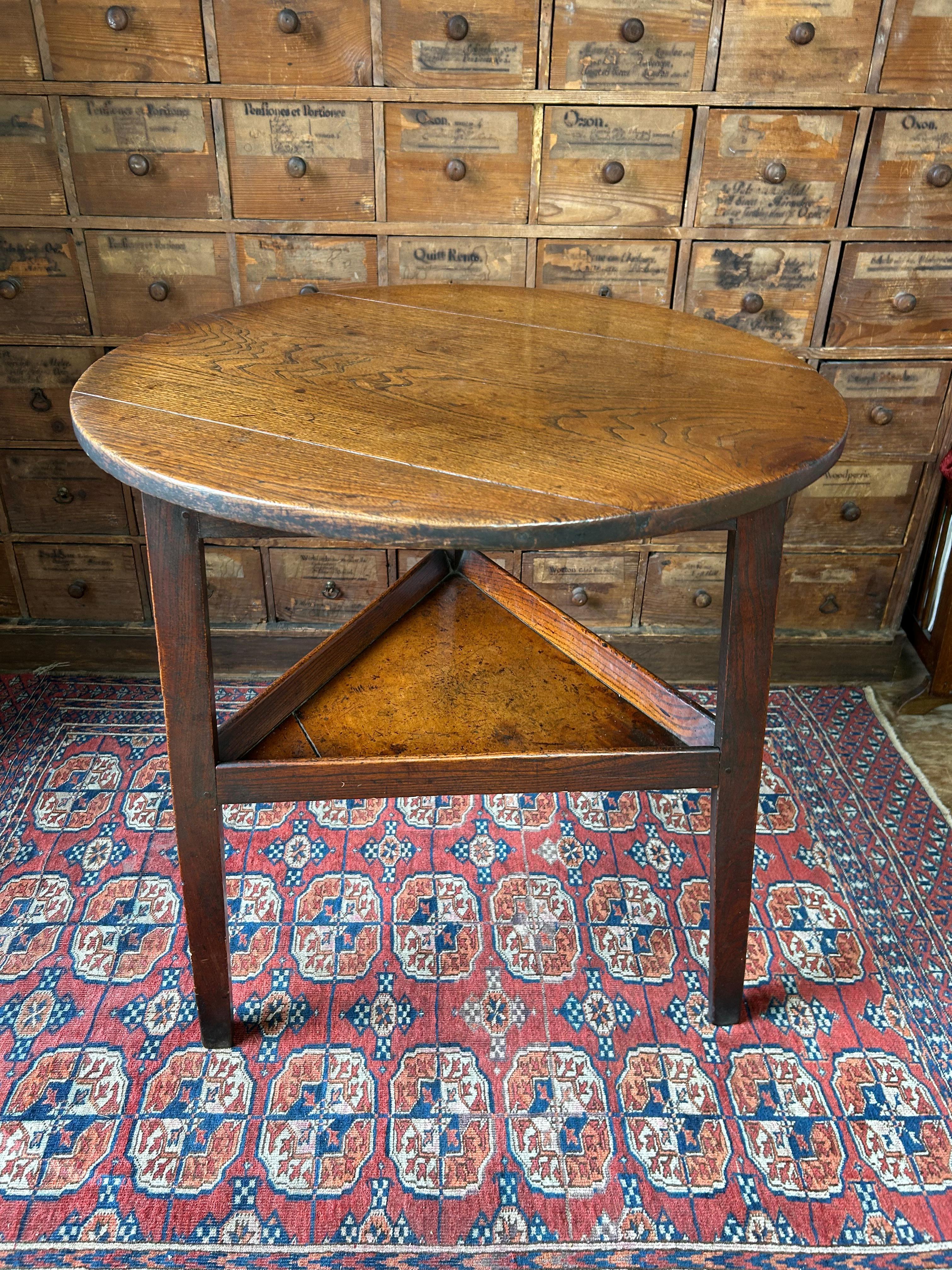 An attractive English Late 18th century Elm and fruitwood cricket table. The three plank elm top rests on a diamond freize, with three slightly splayed legs connected to a lower tier shelf with an angled gallery. The lower shelf base is made from