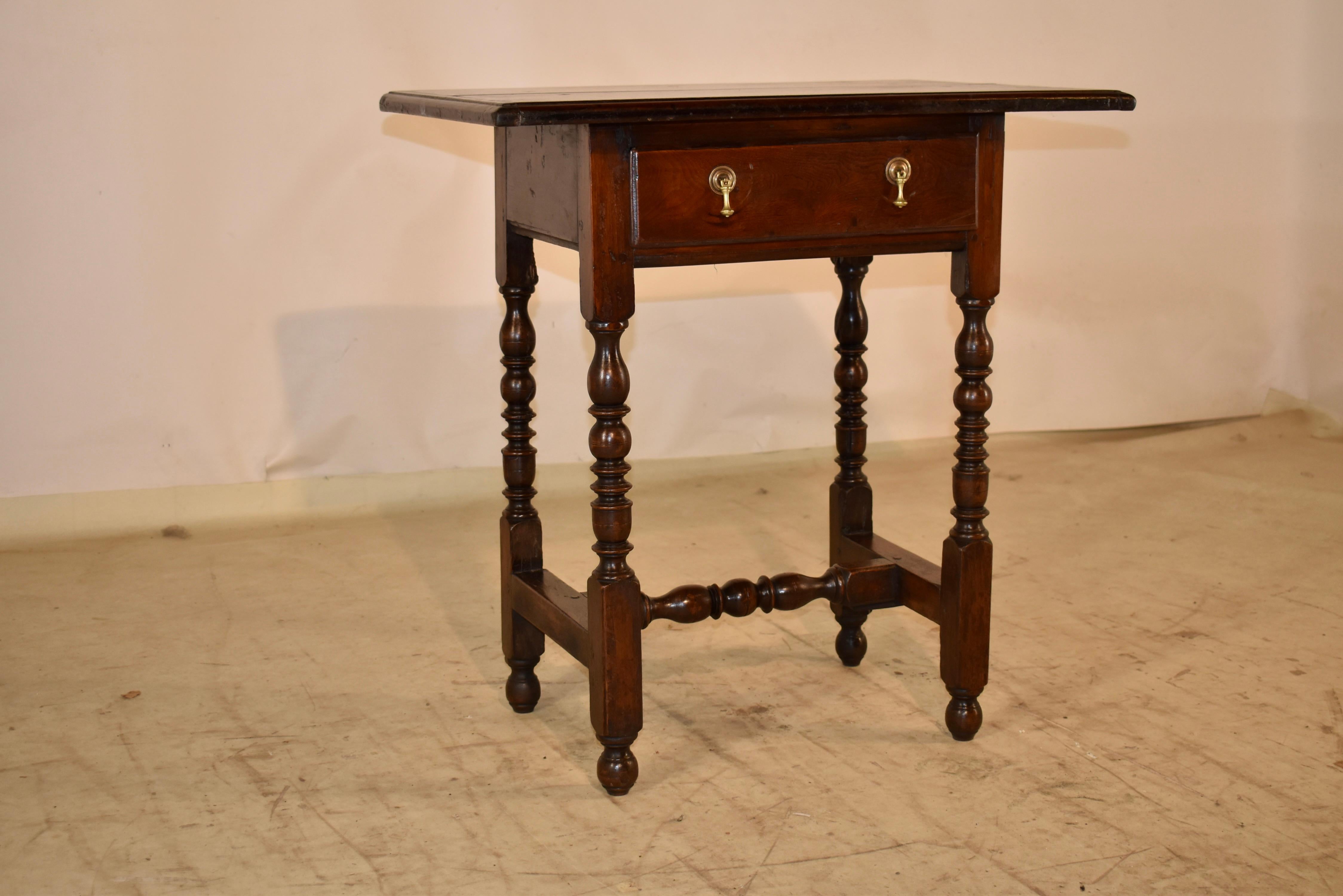 Early 18th century side table from England and made from elm.  The top has a beveled edge, and follows down to a simple apron which contains a single drawer.  The table is supported on hand turned legs, connected by  simple side stretchers and a