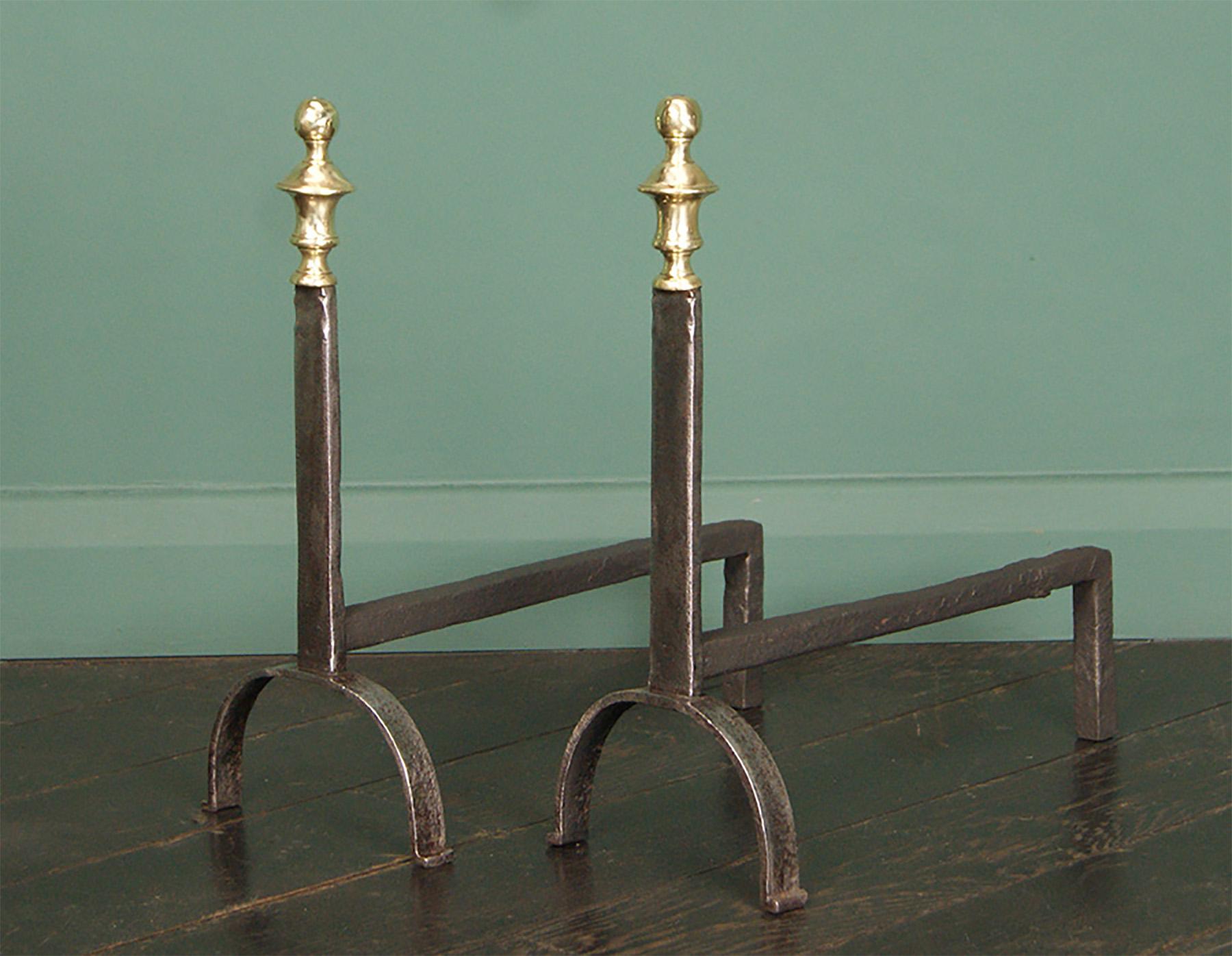 A fine pair of petit 18th century English fire dogs/andirons.  Brass riveted-through urn finials on simple wrought standards with notch decoration on the top, supported on high arched supports.  Stamp to rear with crown.
Restored.

Circa 1730