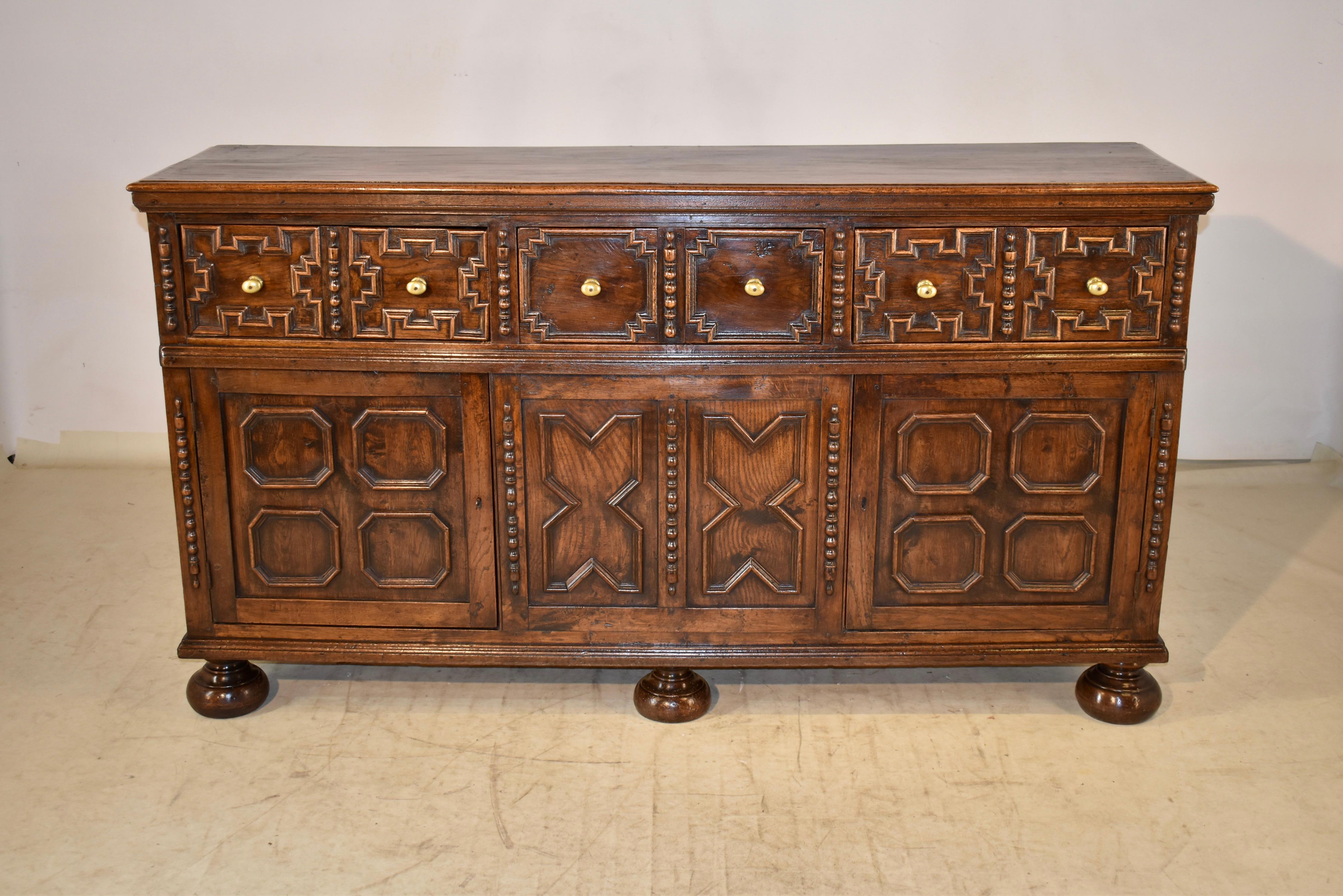 18th century oak dresser base from England. The top is made from a single oak plank, and has a beveled edge. The sides are hand paneled, and the front of the case has three drawers, all with raised geometric paneled drawer fronts, flanked by
