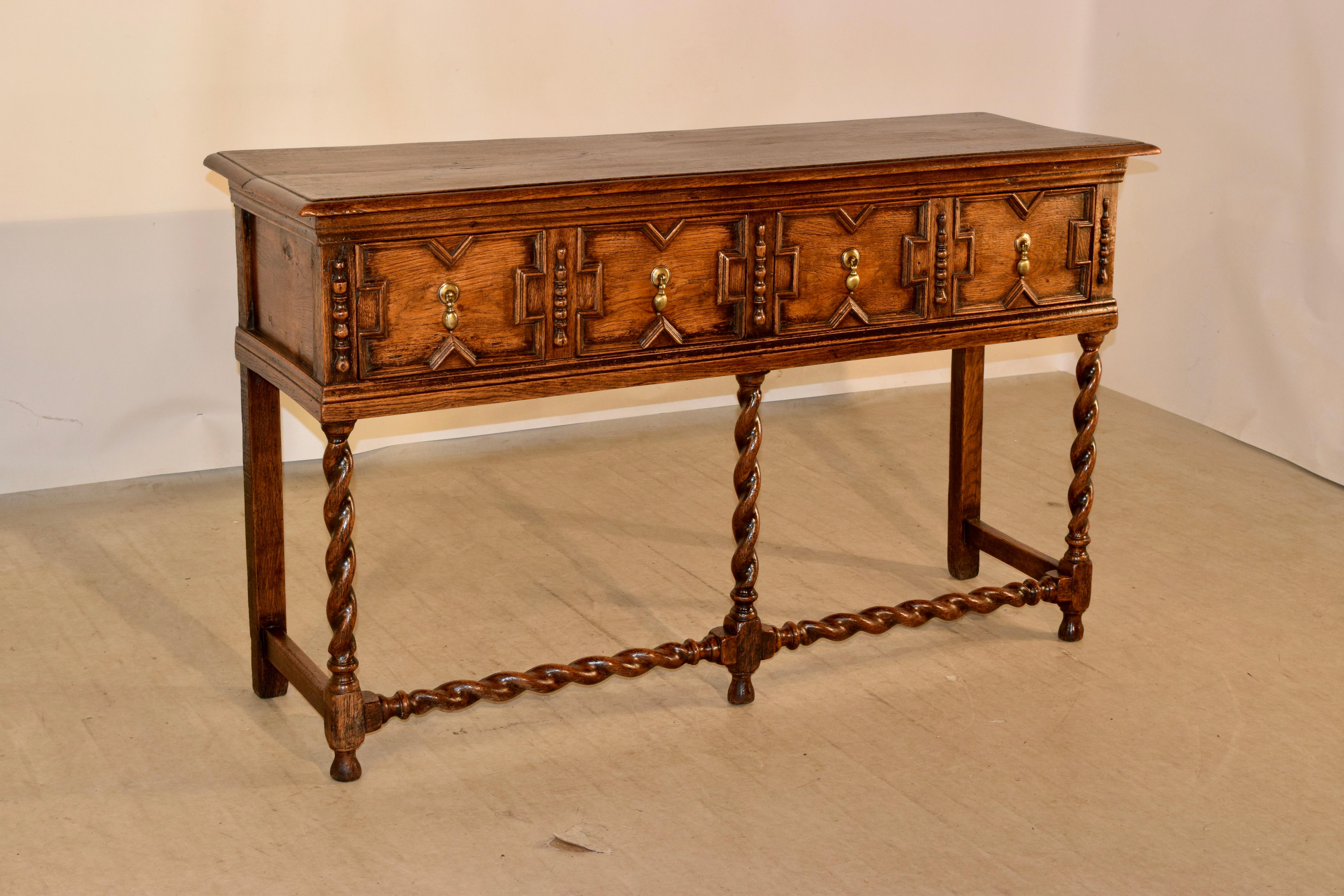 18th century oak sideboard from England with a single plank top, which has a beveled edge, following down to simple paneled sides and two drawers in the front with raised geometric patterned drawer fronts, flanked by applied half turnings. The case
