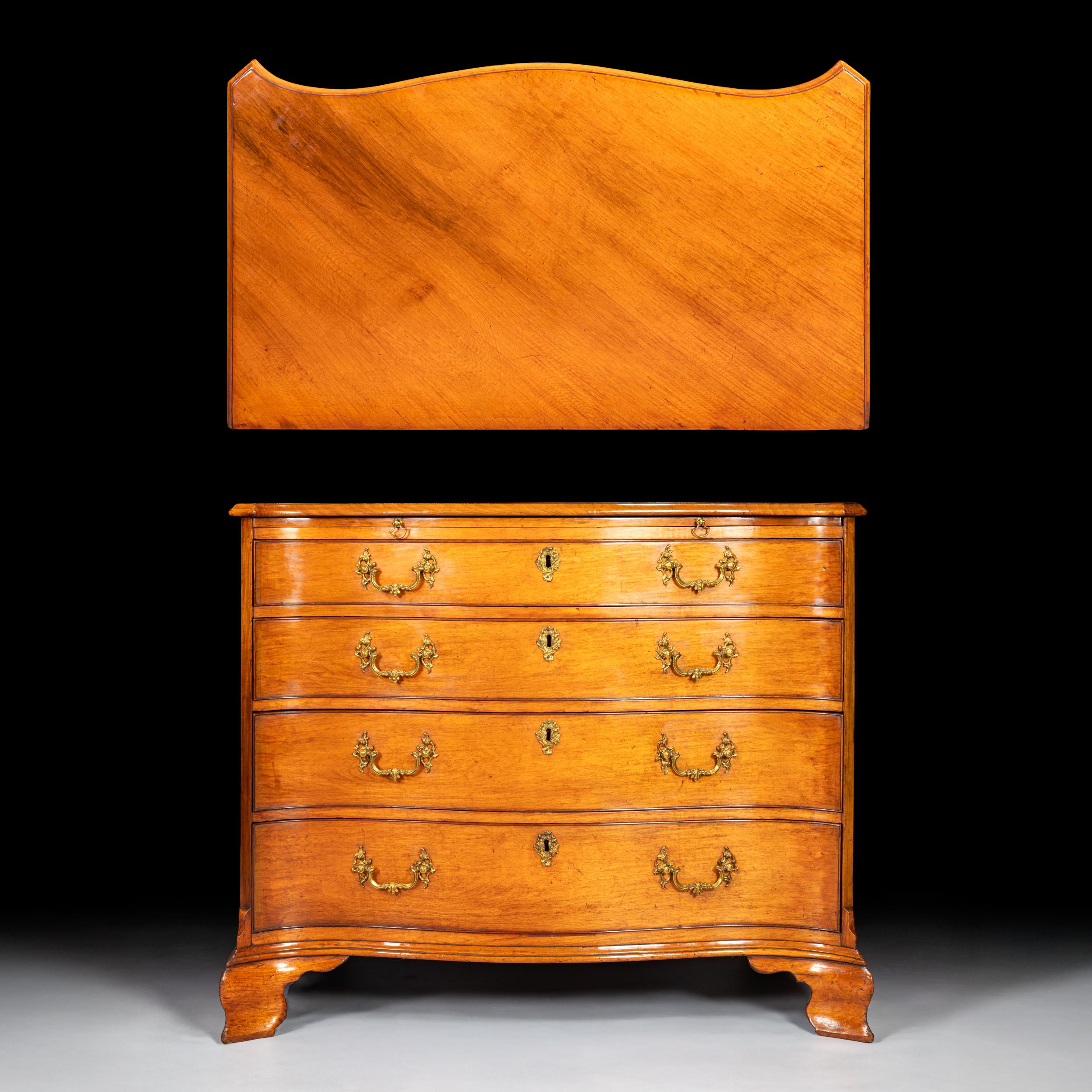 A fine George III period serpentne fronted chest of drawers with carved molded top edge. A full-length brush slide sits above four long drawers. The piece is complete with original swan neck brass handles and terminates on ogee bracket feet. A fine