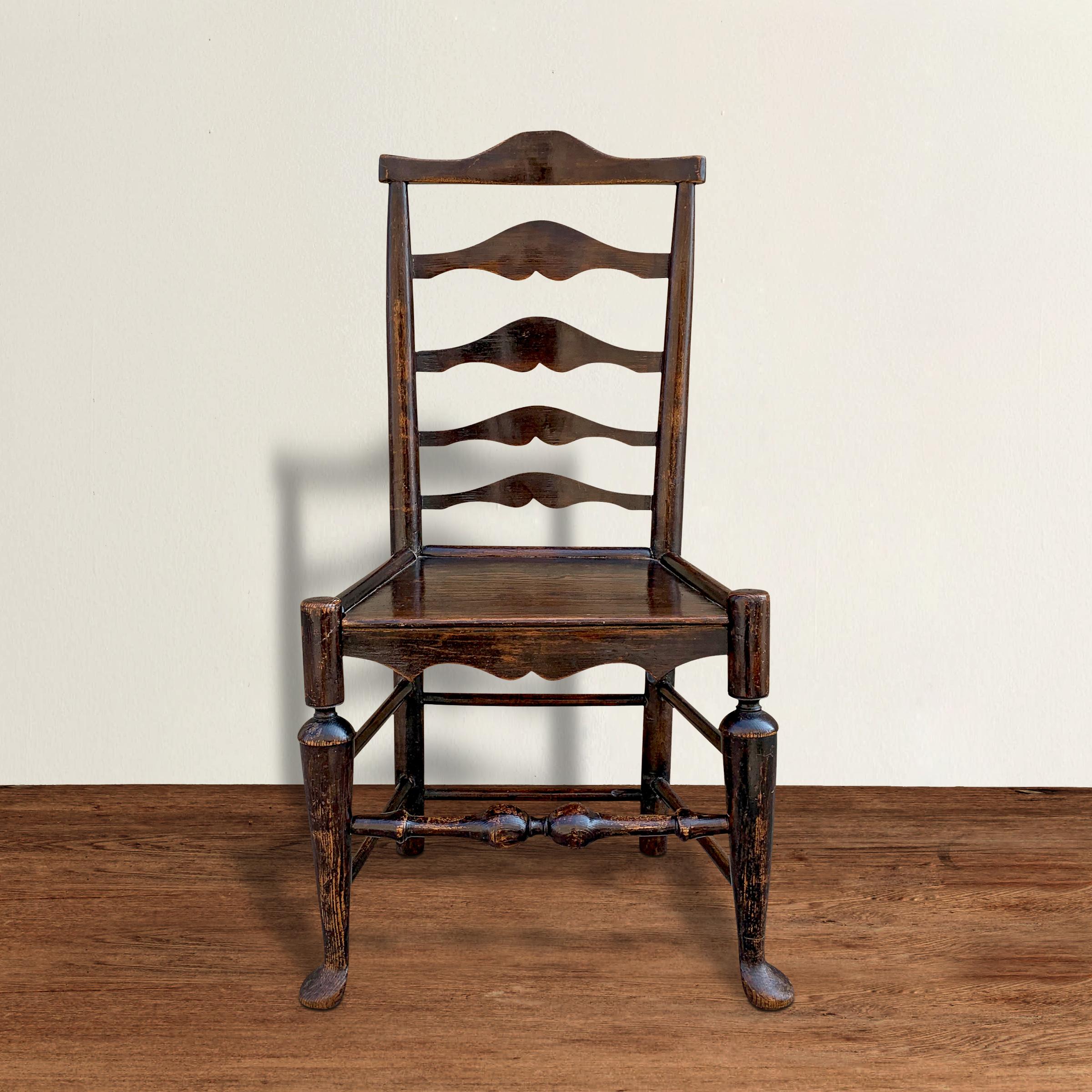 A fantastic 18th century English George III ladder-back oak side chair with beautiful details including curved backsplats, a solid plank seat, trumpet turned legs ending in out-turned pad feet, and a beautiful worn turned stretcher in the front. The