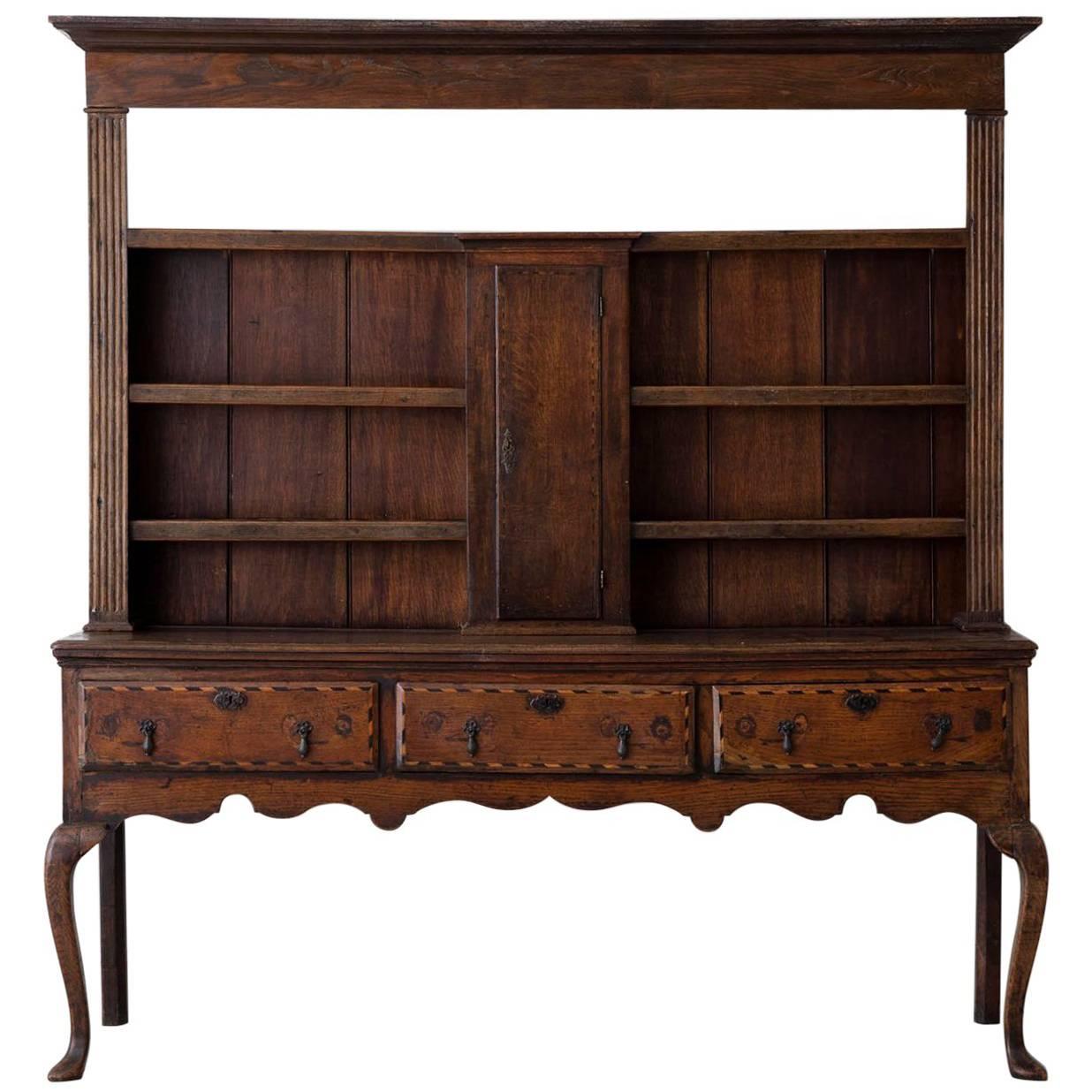 A late 18th century two-part English oak Welsh dresser server or buffet with an exceptional patina from the Georgian period. The upper section has four shelves and a central cupboard door. The lower section has a scalloped apron and three drawers