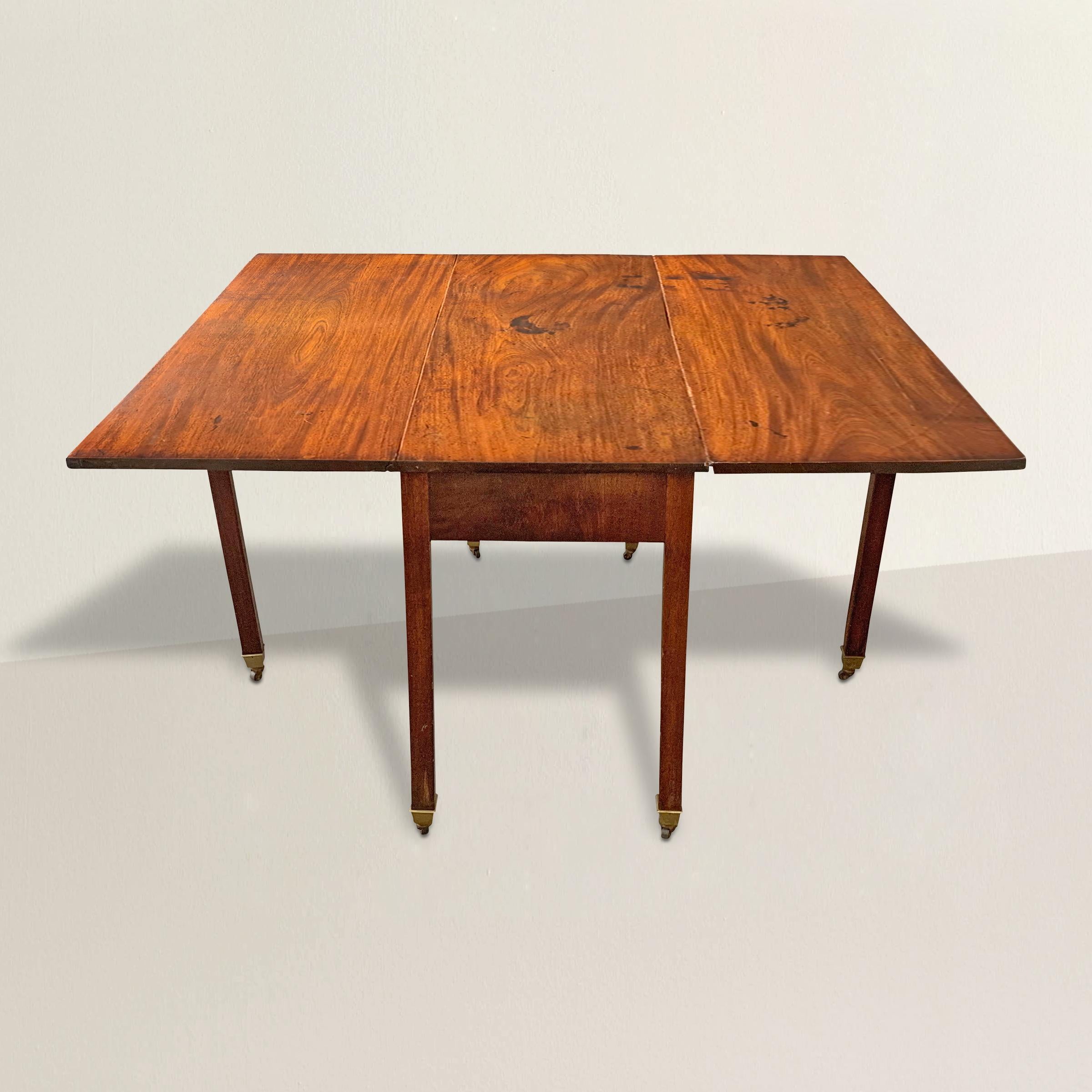 A chic and modern-in-spirit 18th century English Georgian mahogany drop-leaf gate-leg breakfast table with a top made from three solid planks of mahogany and tapered square legs ending with brass-mounted iron casters. This table is very versatile