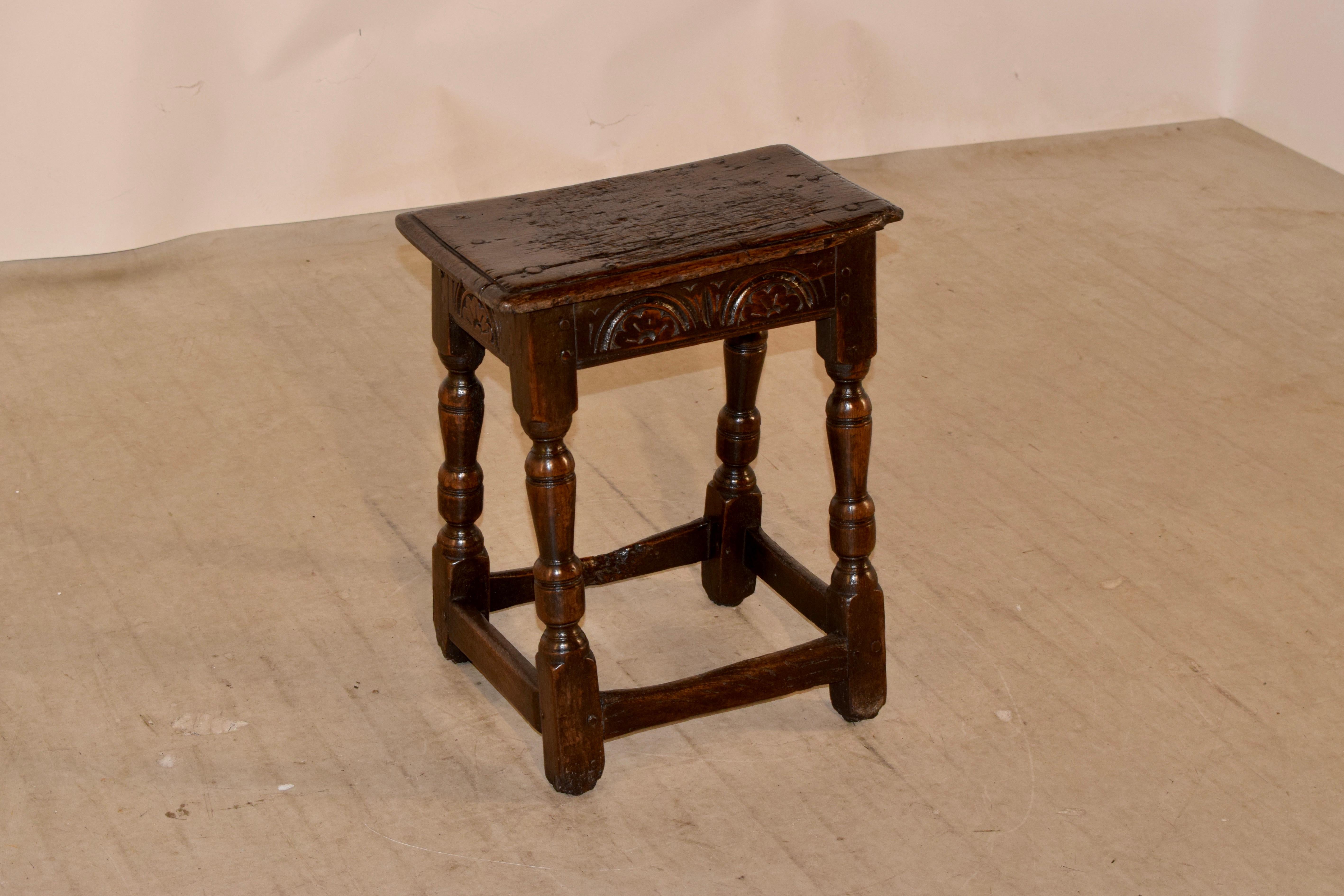 18th century oak joint stool from England with a beveled edge around the top, following down to a hand carved decorated apron, supported on hand turned legs, joined by simple stretchers, which are deliciously worn from age and use.