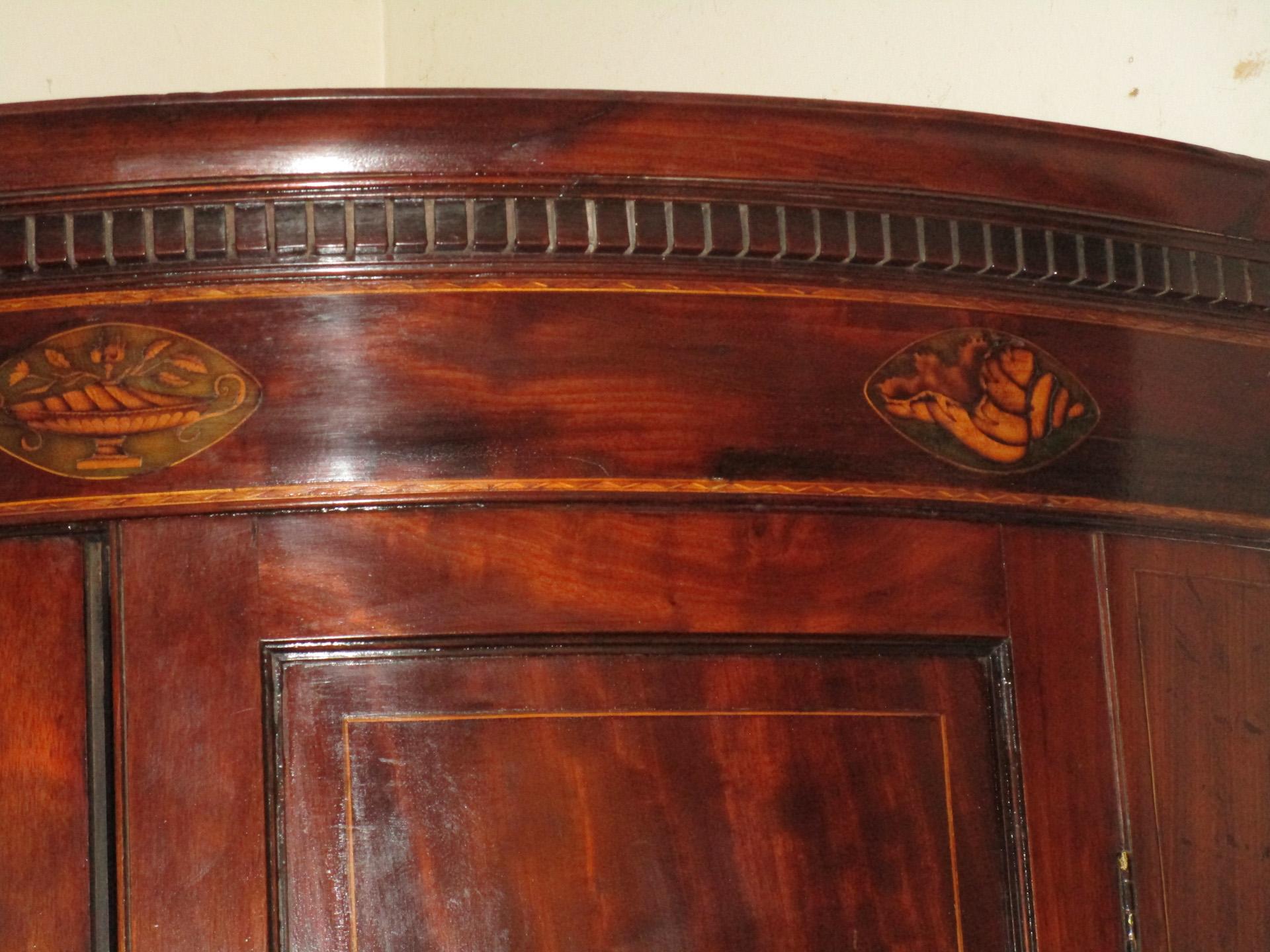 Late 18th century English mahogany bowfront hanging cupboard featuring string inlay on the doors with bone escutcheons, three curved interior drawers with brass pulls and four interior shelves. The intricate fruitwood inlay at the top of the cornice